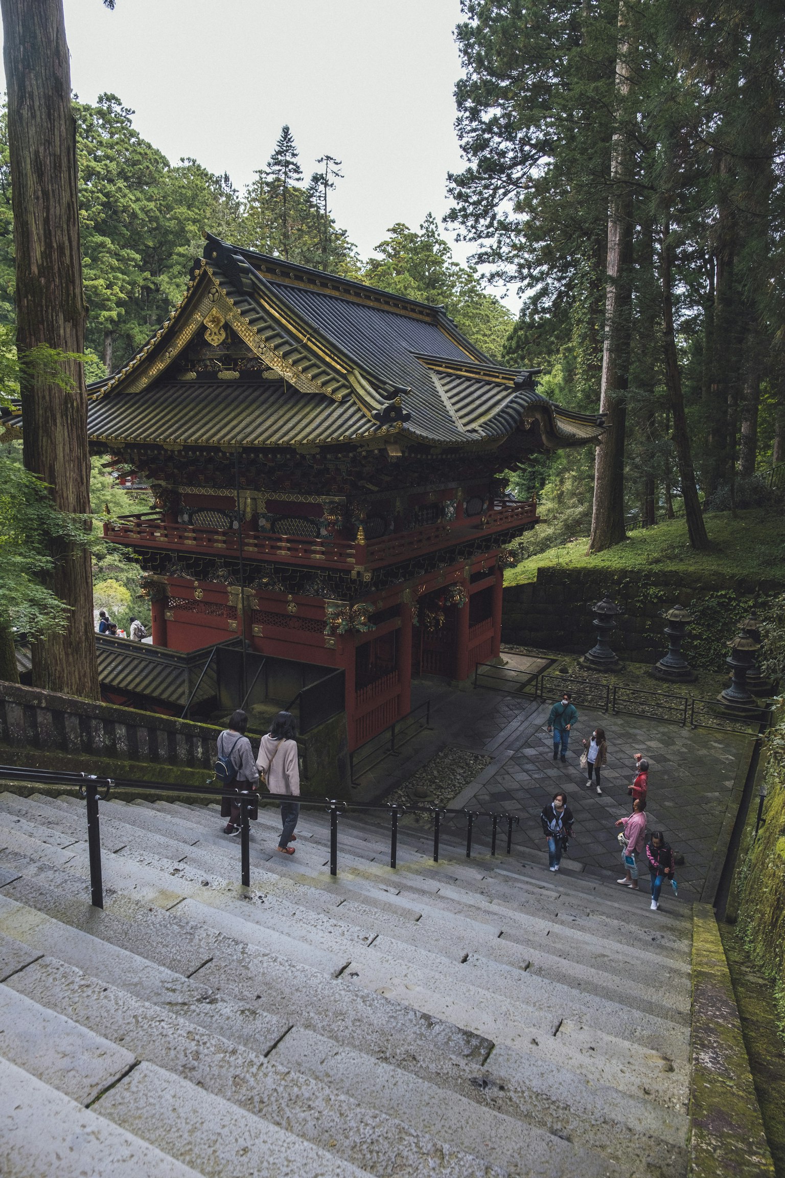 People descending stone steps near a historic temple surrounded by lush greenery