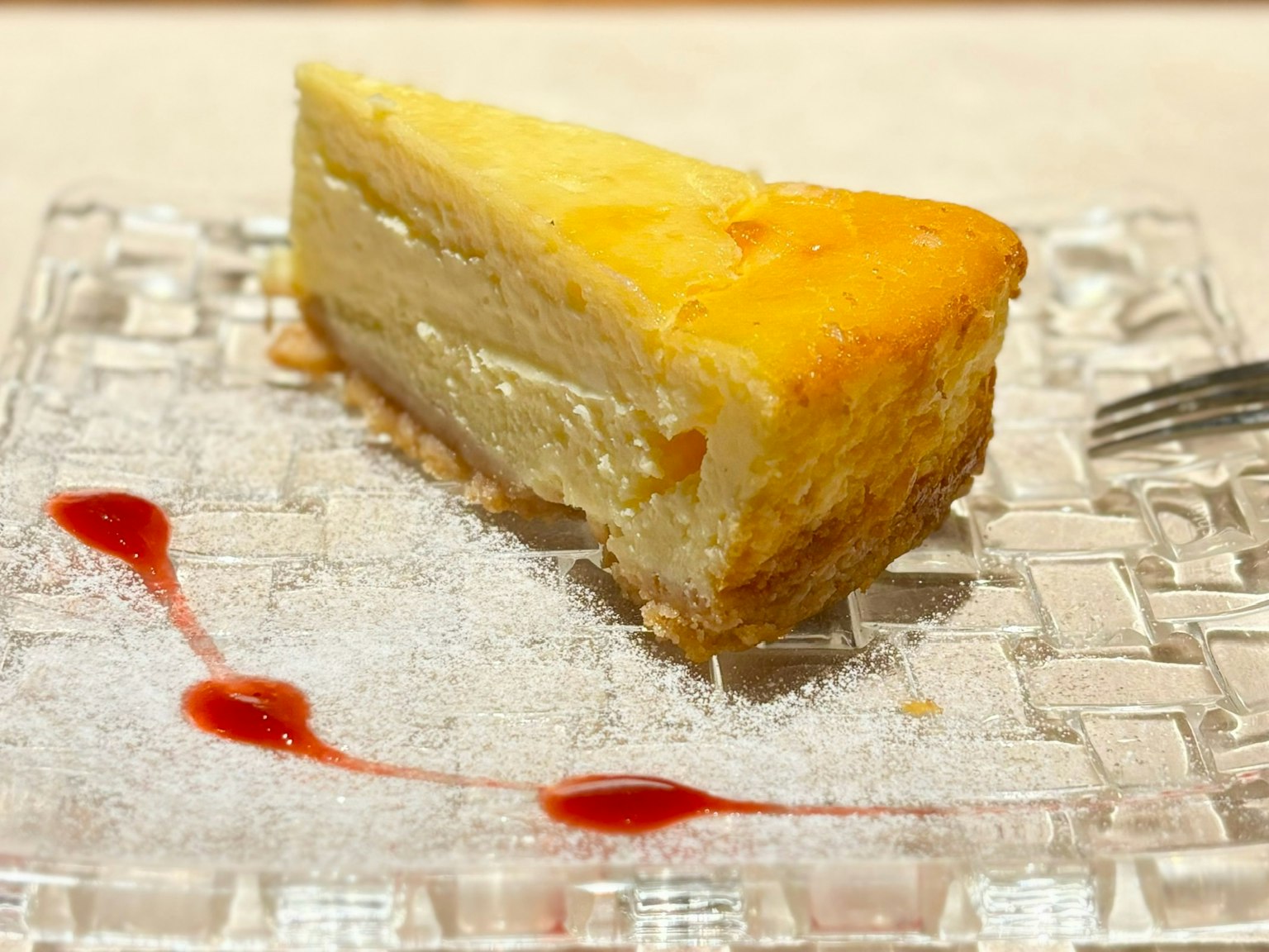 Fetta di cheesecake cremosa servita su un piatto trasparente con un filo di salsa di lamponi