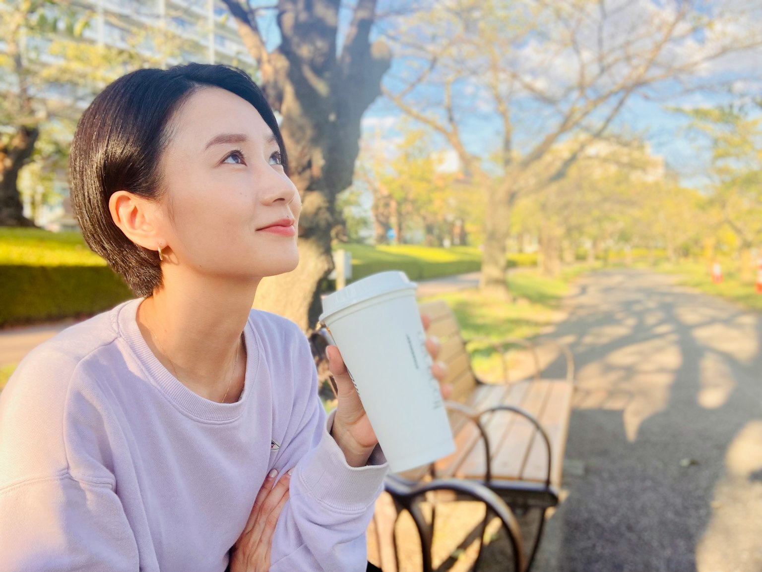 Người phụ nữ cầm cốc cà phê suy tư trong công viên