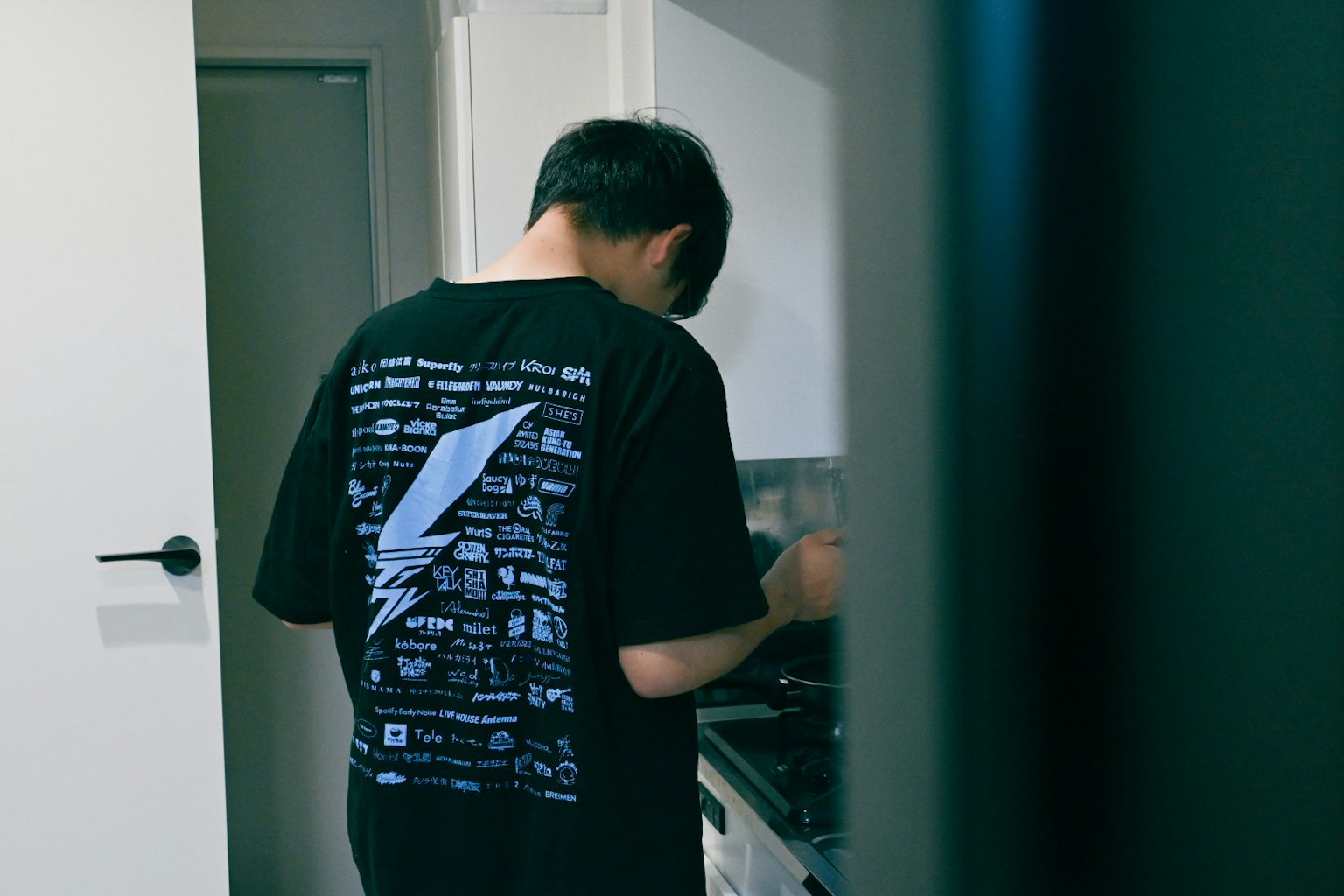 厨房里做饭的人背面黑色T恤印有图形设计白色门背景