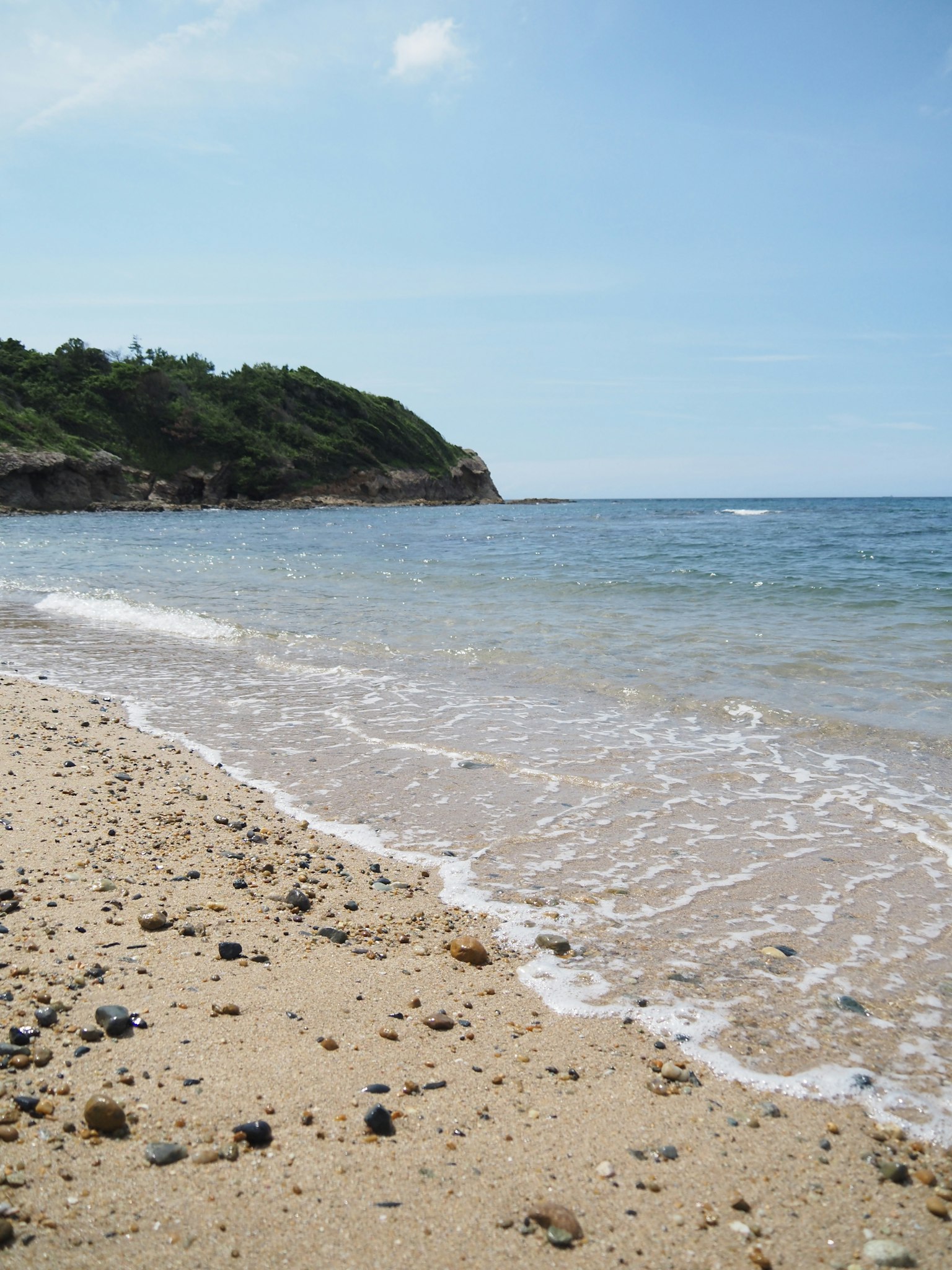 Pantai berpasir dengan ombak lembut dan langit biru jernih