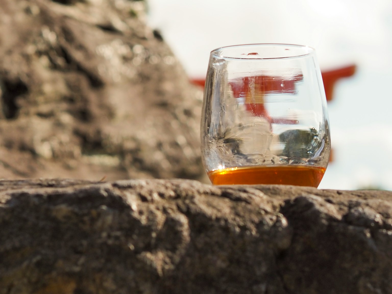 A transparent glass with orange drink placed on a rock with a torii gate in the background