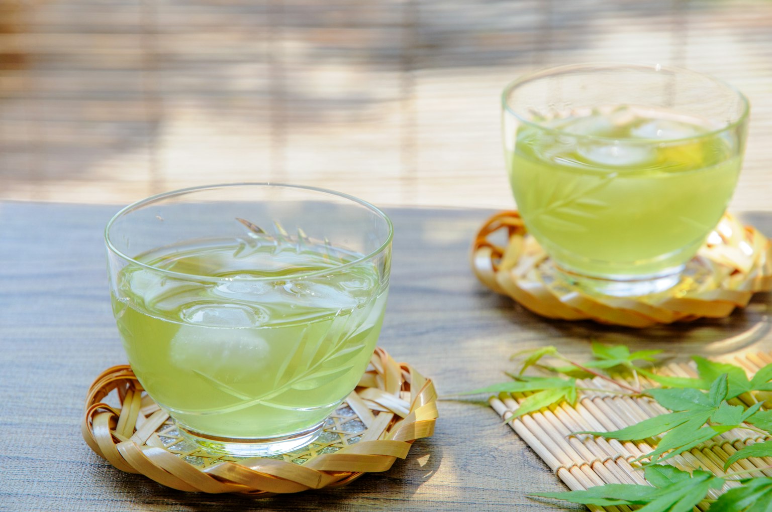 Two glasses of iced green tea on bamboo coasters