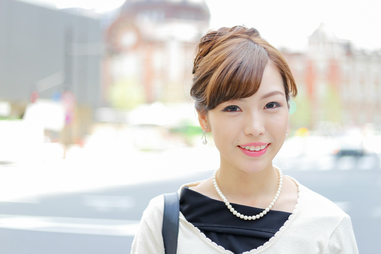ผู้หญิงวัยหนุ่มยืนอยู่หน้าพื้นหลังสว่างยิ้มใส่สร้อยคอไข่มุก