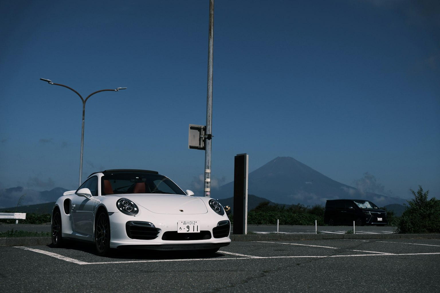 Porsche putih diparkir di bawah langit biru dengan gunung di latar belakang