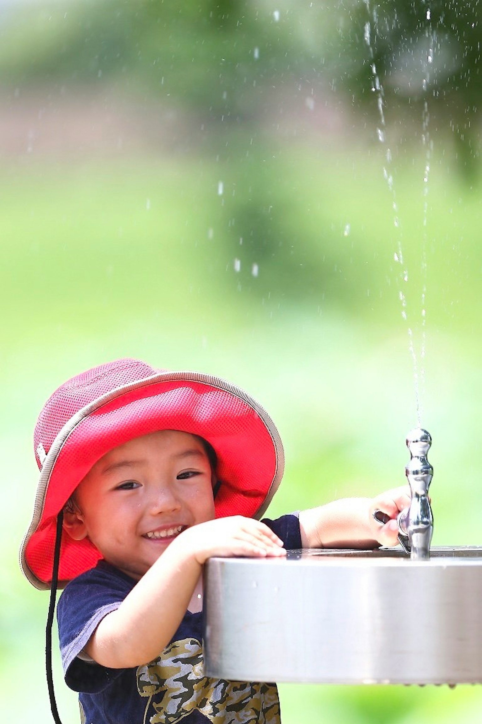 Niño sonriente en una fuente de agua con un sombrero rojo salpicando agua