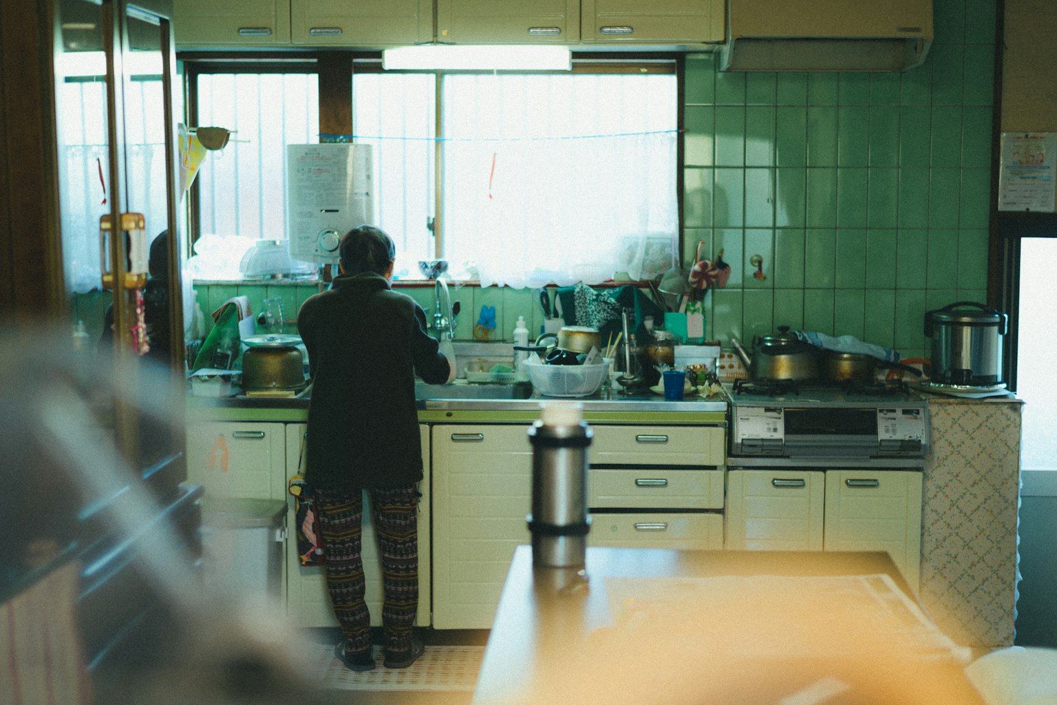 緑のタイルのキッチンで料理をする高齢の女性