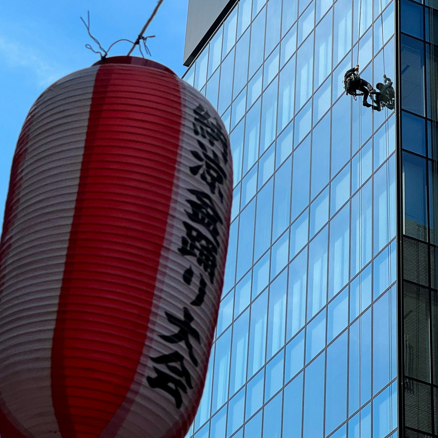 Linterna roja y blanca con limpiadores de ventanas en un rascacielos
