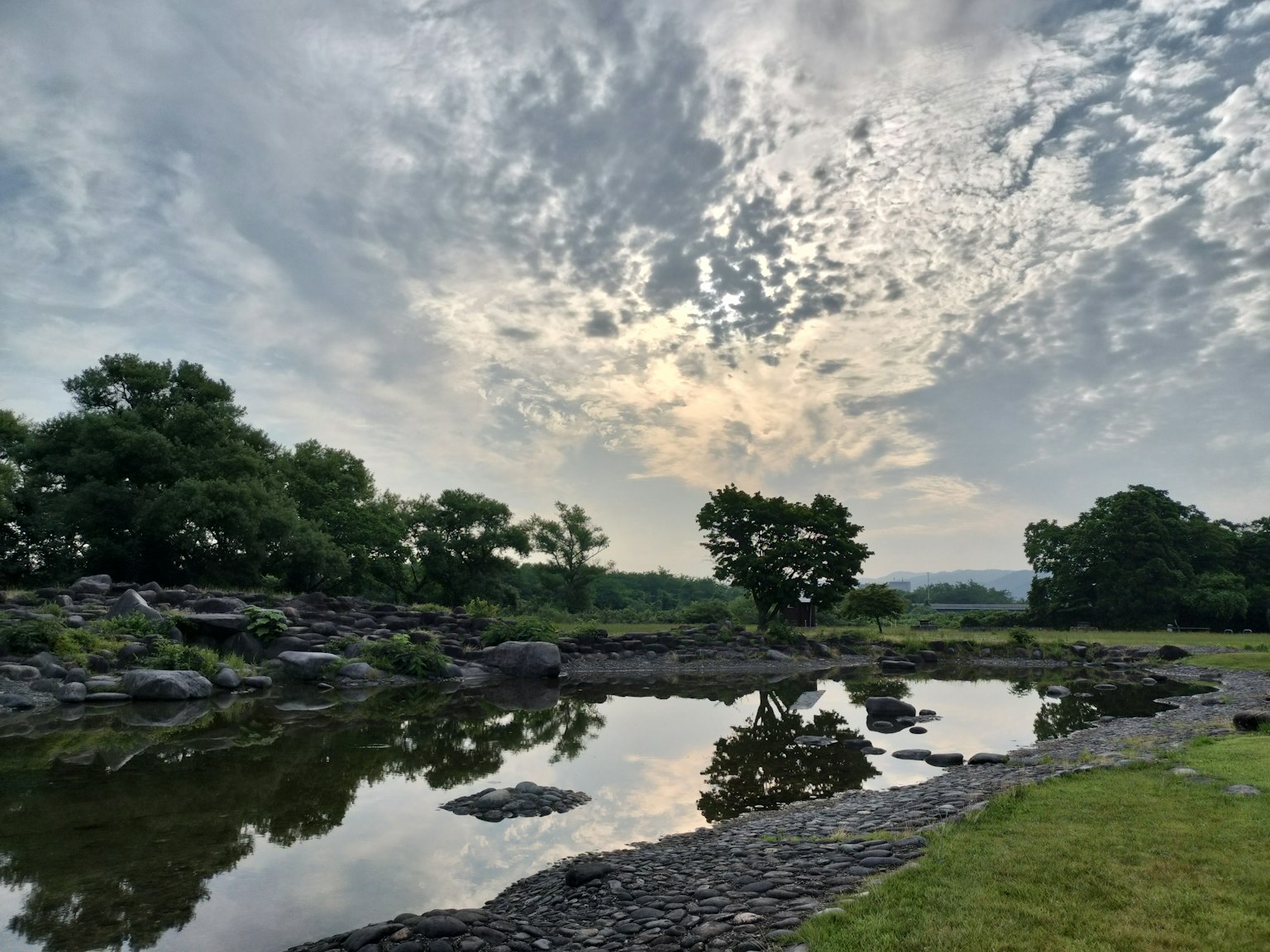 Ruhige Flusslandschaft mit grünen Bäumen und bewölktem Himmel, der sich im Wasser spiegelt