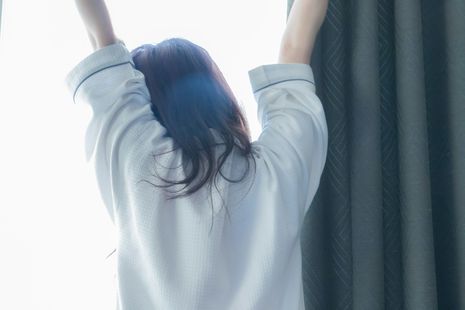 Woman stretching and opening curtains in a bright room