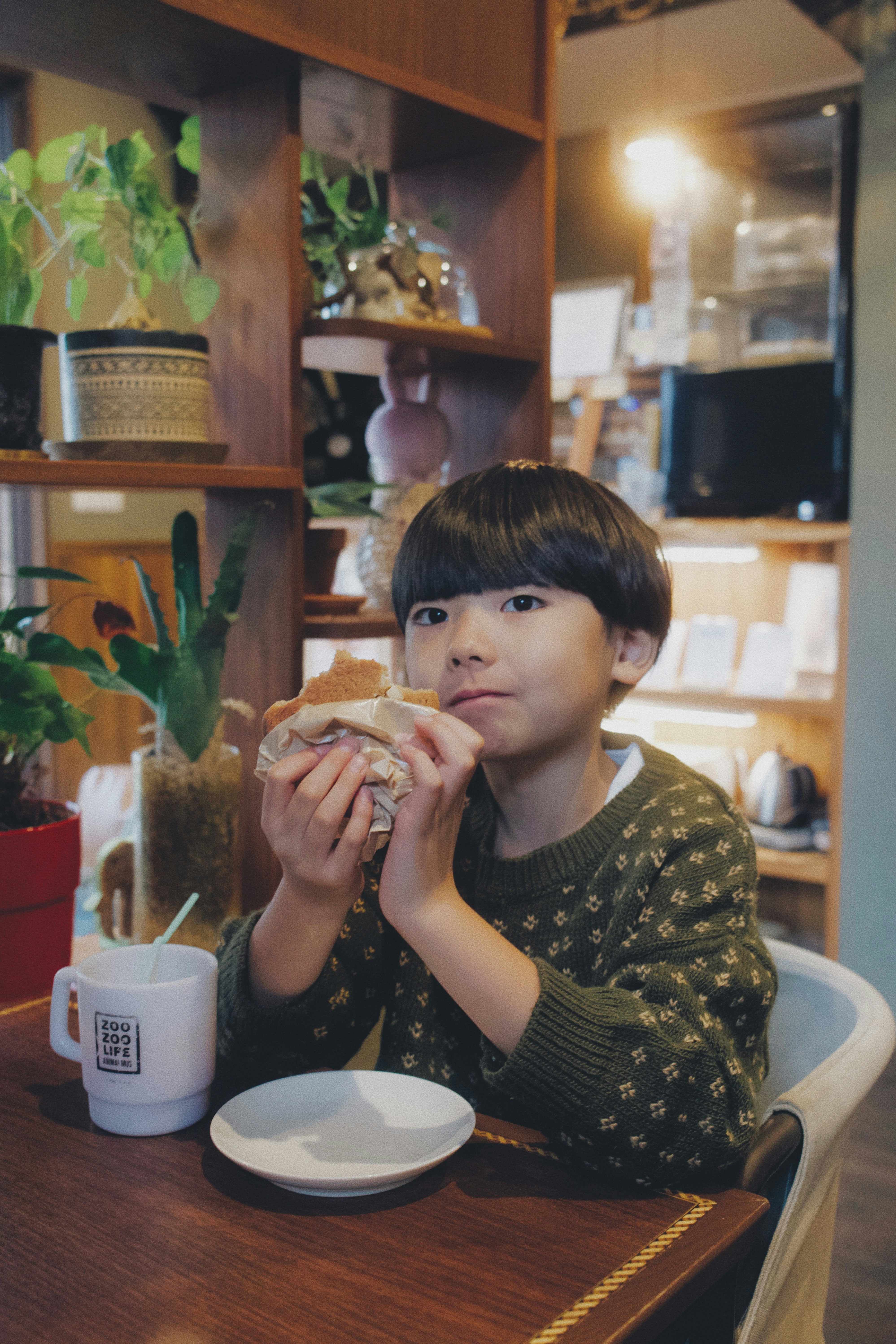 Un niño sentado en una mesa de cafetería sosteniendo pan