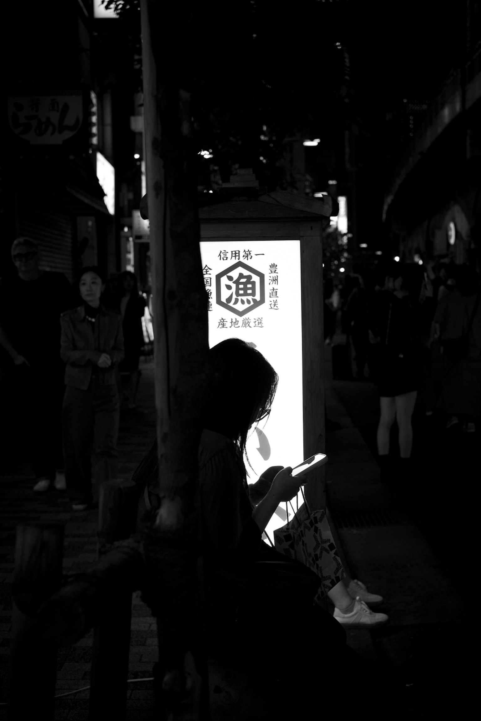 Silhouette di una persona seduta che usa uno smartphone in una strada buia con un'insegna luminosa