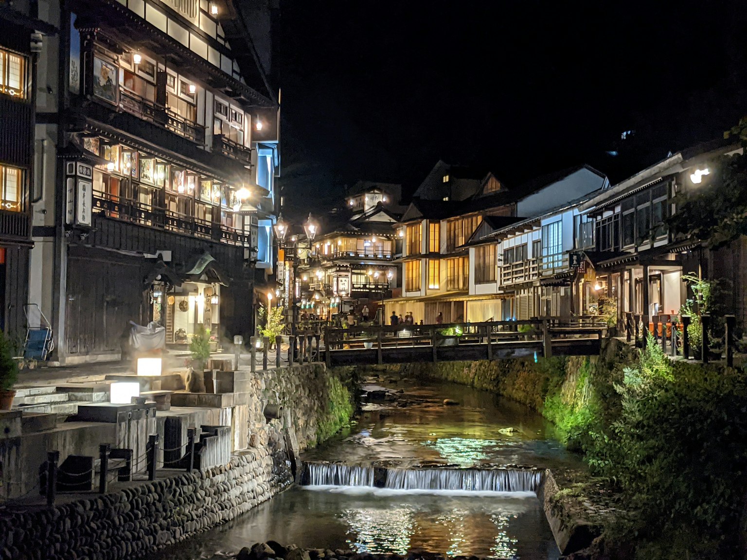 Vista panoramica di una città termale di notte con edifici tradizionali lungo un fiume e un ponte