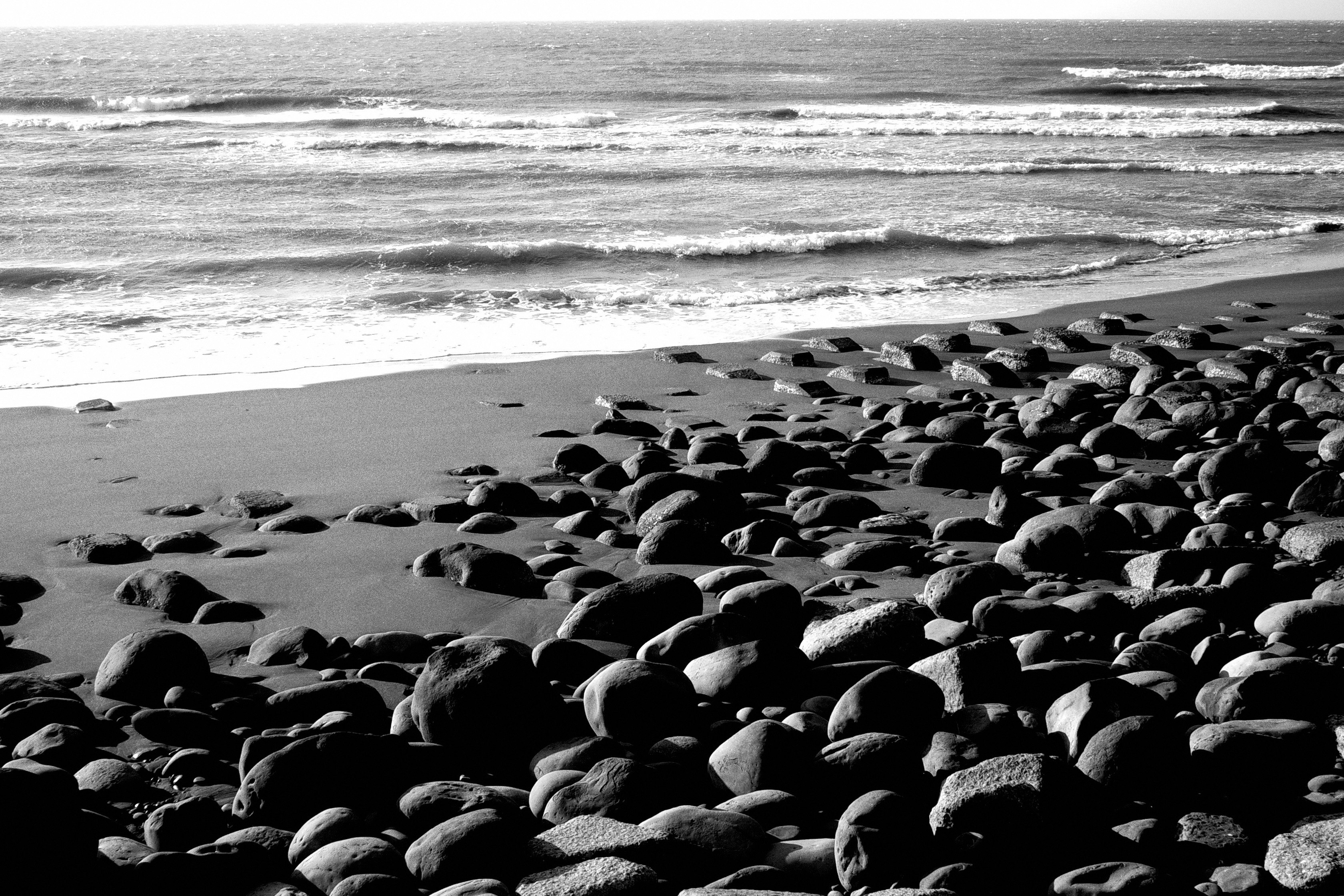 orilla rocosa con olas y playa de arena
