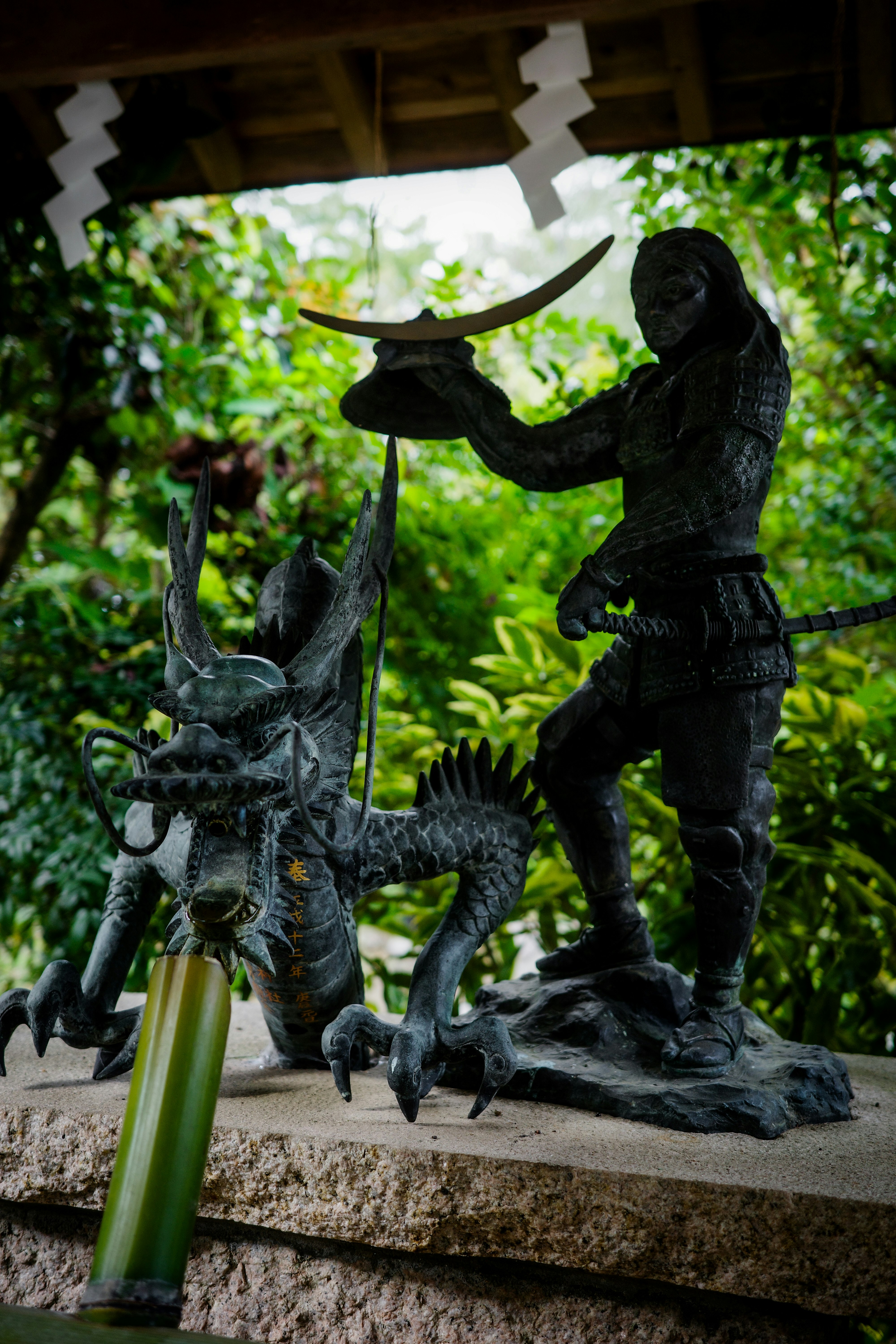 sculpture de statue en bronze sur un socle en pierre avec une fontaine dans un jardin vert