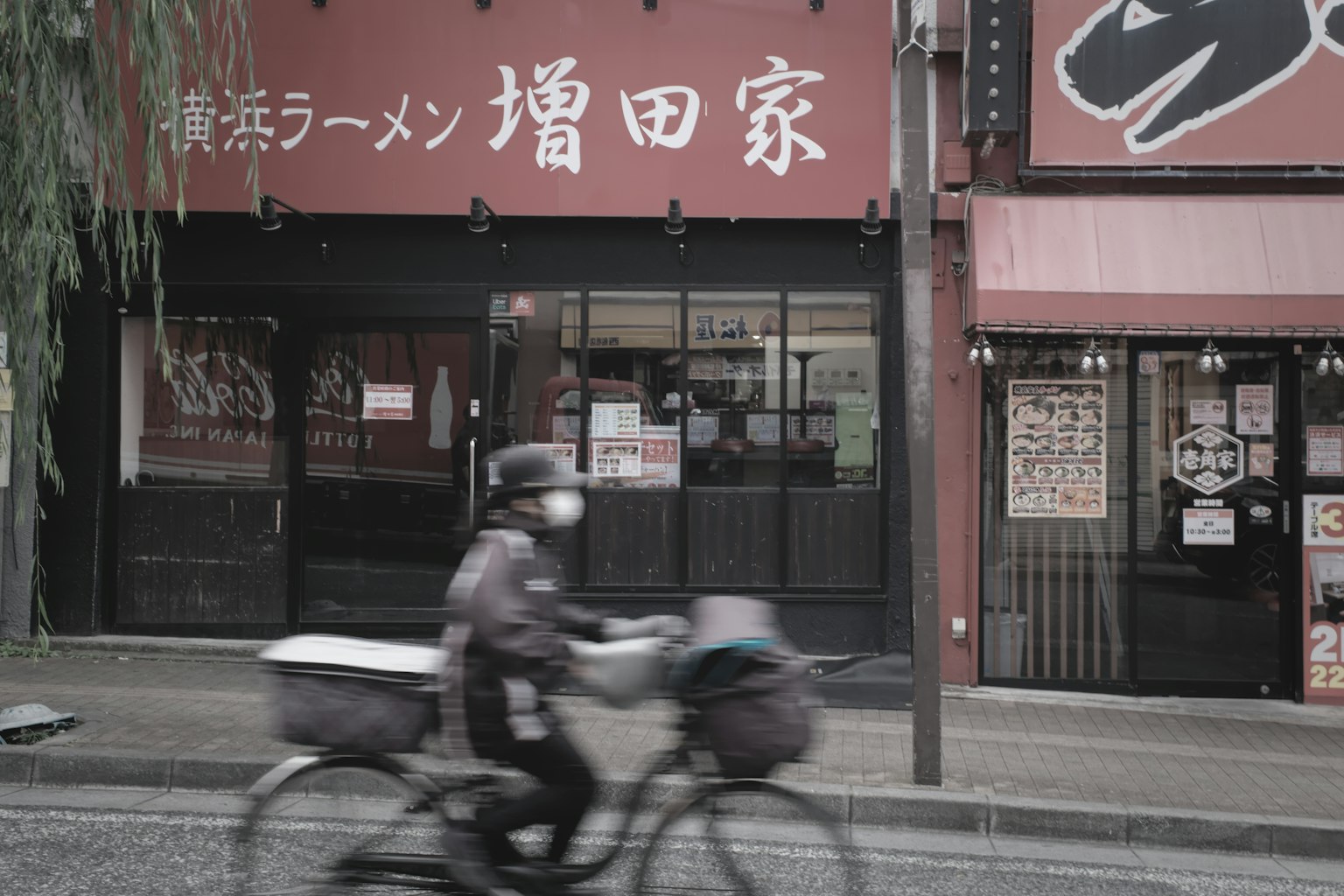 一幅捕捉騎自行車的人在拉麵店前的圖像