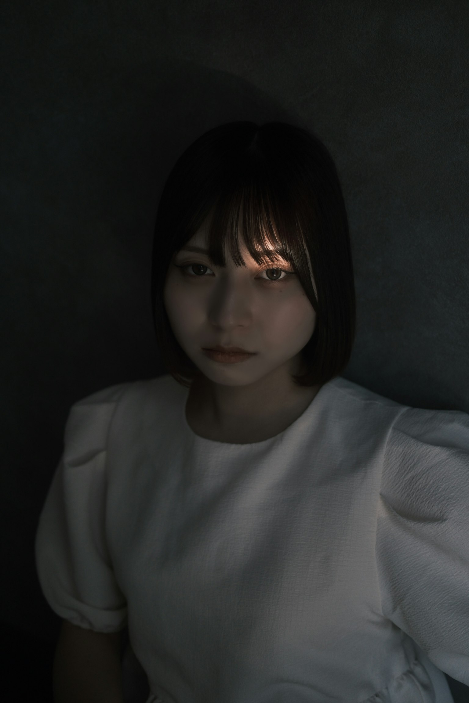 暗い背景に白い服を着た女性のポートレート 照明が彼女の顔に当たっている