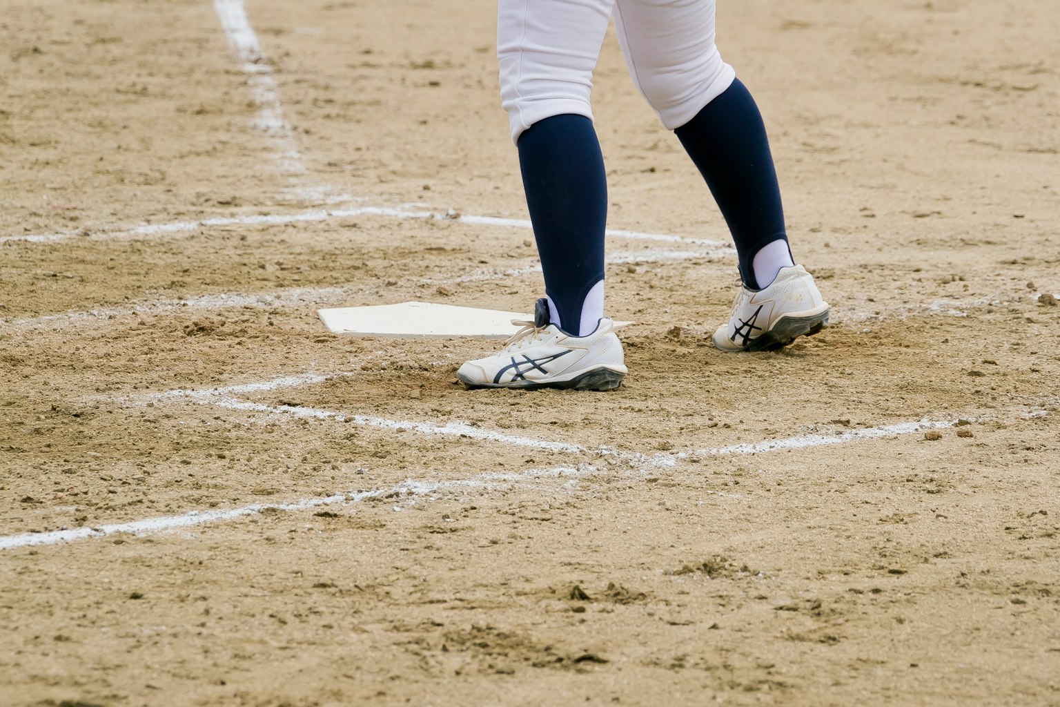 Primo piano dei piedi di un giocatore su un campo da baseball con scarpe bianche e calze blu navy
