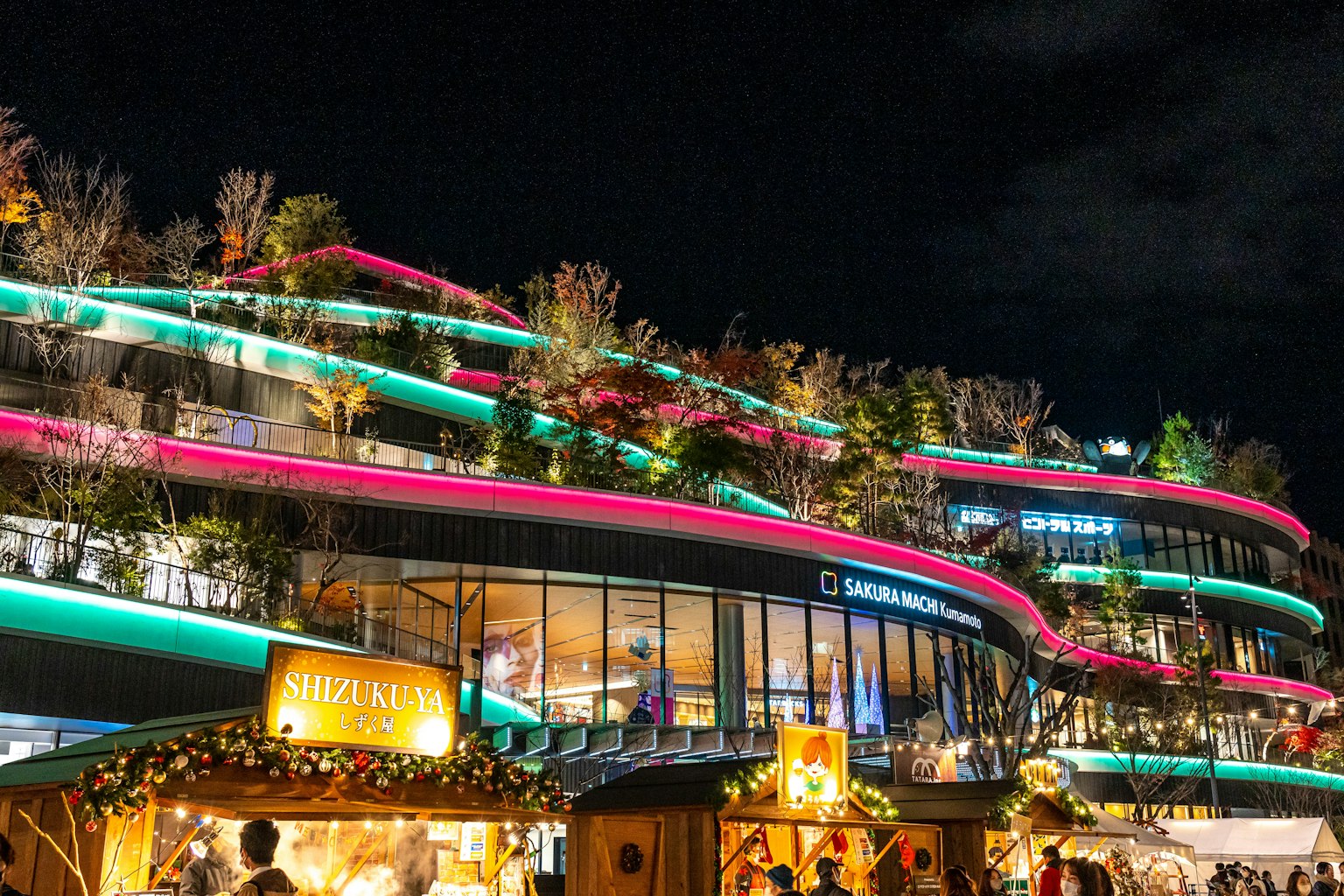 Bâtiment moderne illuminé la nuit avec des lumières colorées et des stands environnants