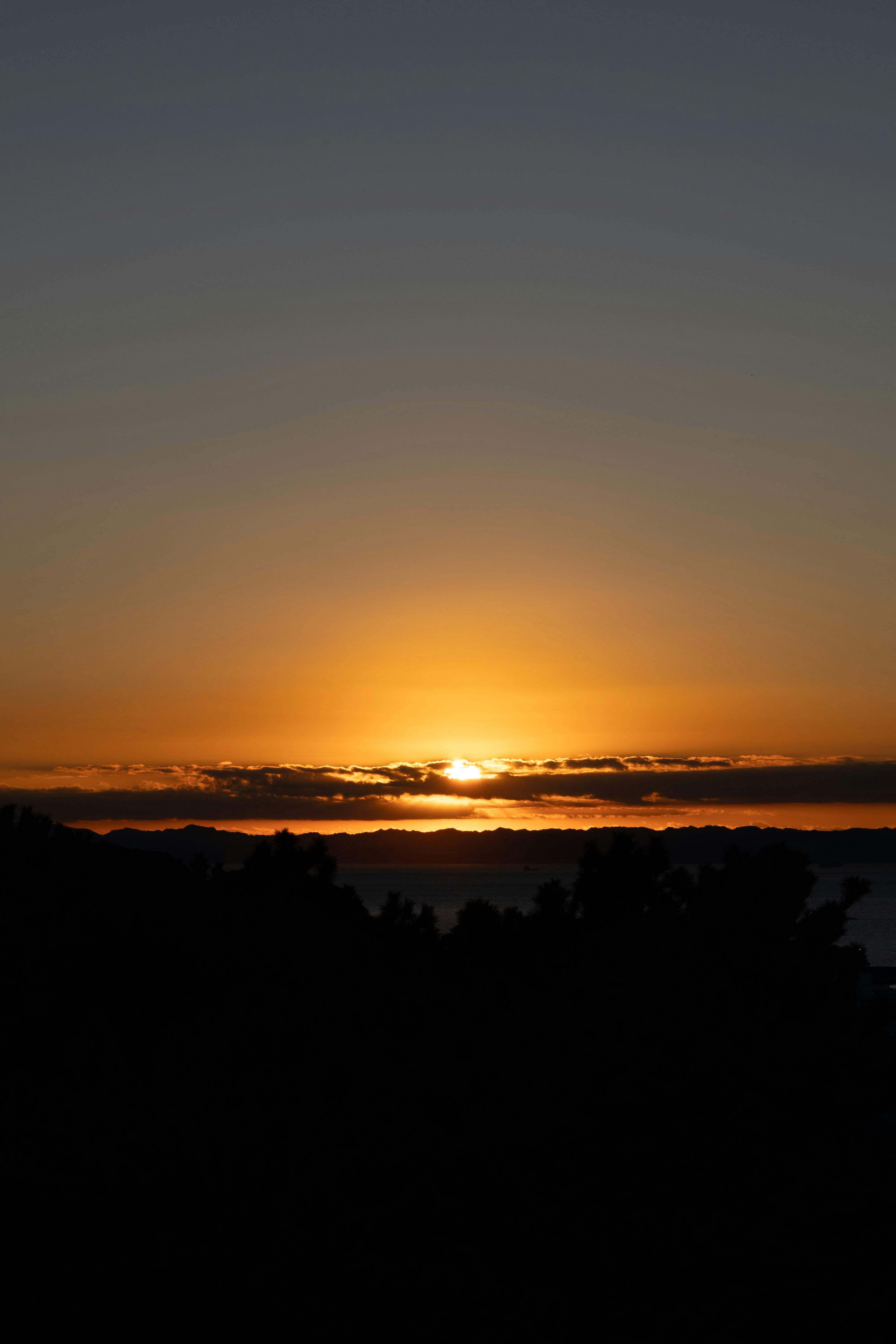 夕焼けの水平線と雲のシルエットが広がる風景