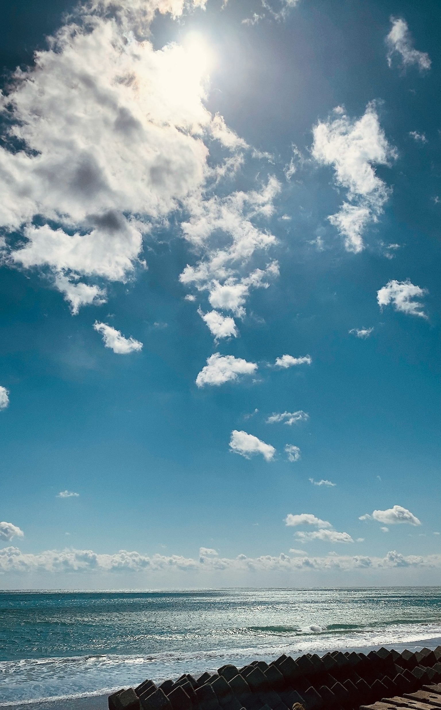Landschaftsblick auf einen blauen Himmel mit weißen Wolken und der Sonne, die über dem Ozean scheint