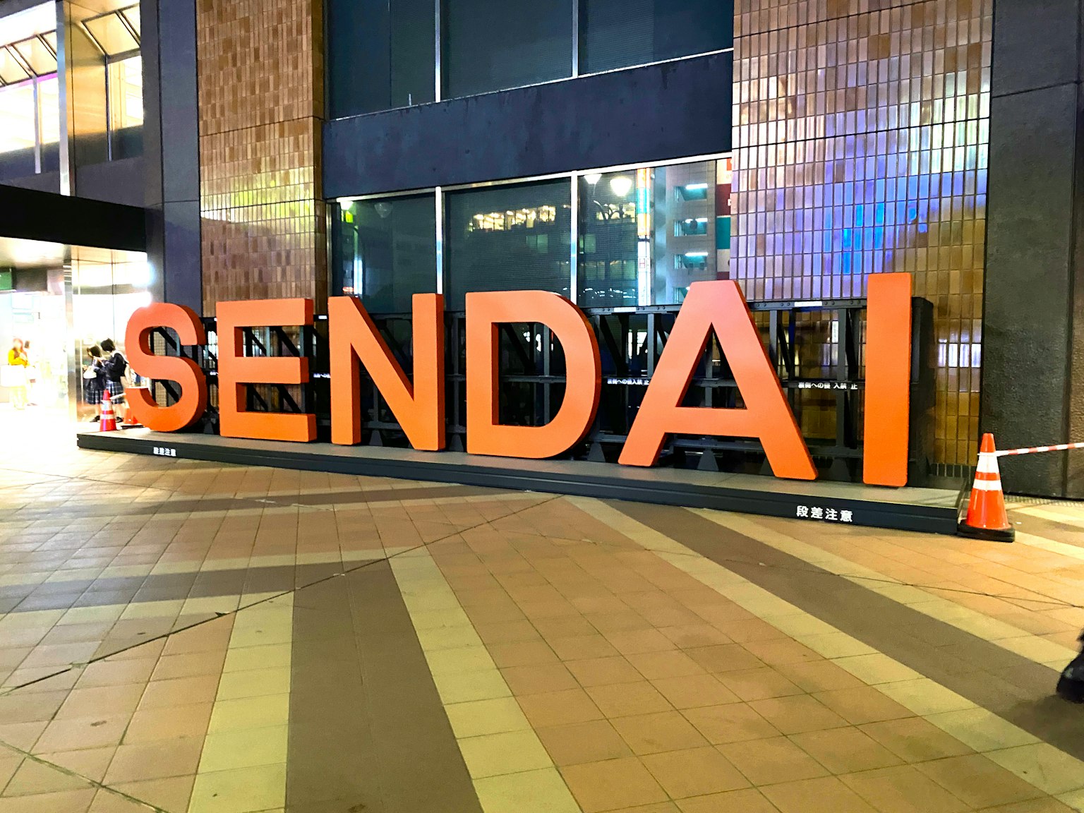 Biển hiệu lớn màu cam hiển thị SENDAI trong bối cảnh thành phố vào ban đêm