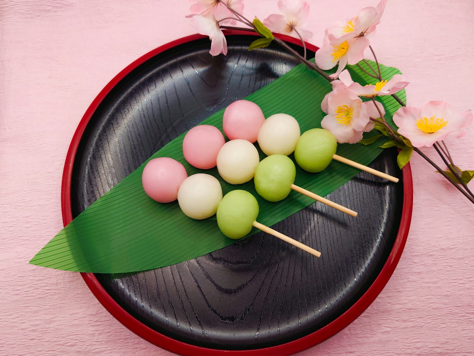 Dango nhiều màu được sắp xếp trên đĩa đen với lá xanh và hoa anh đào