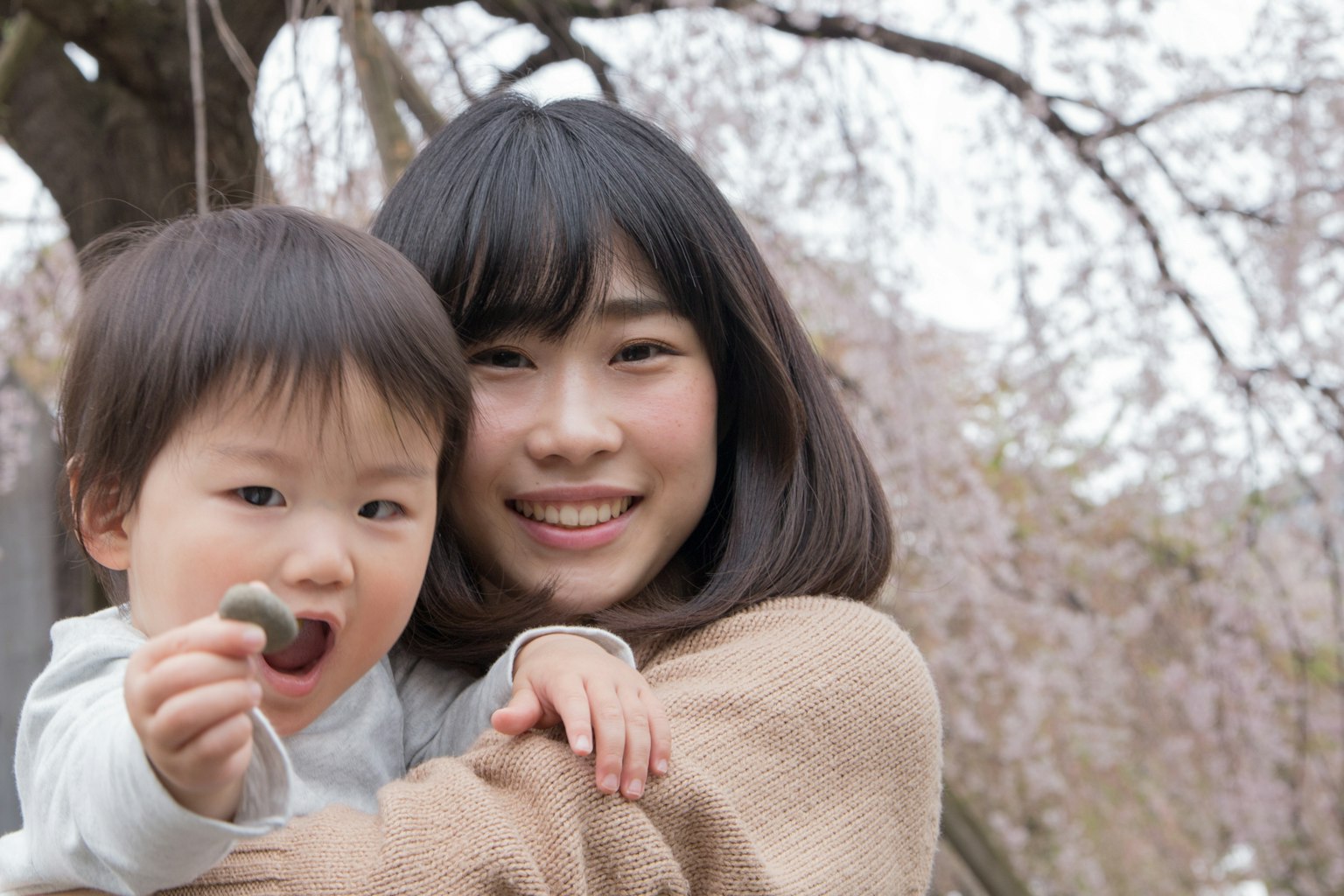 Femme souriante tenant un enfant sous un cerisier en fleurs