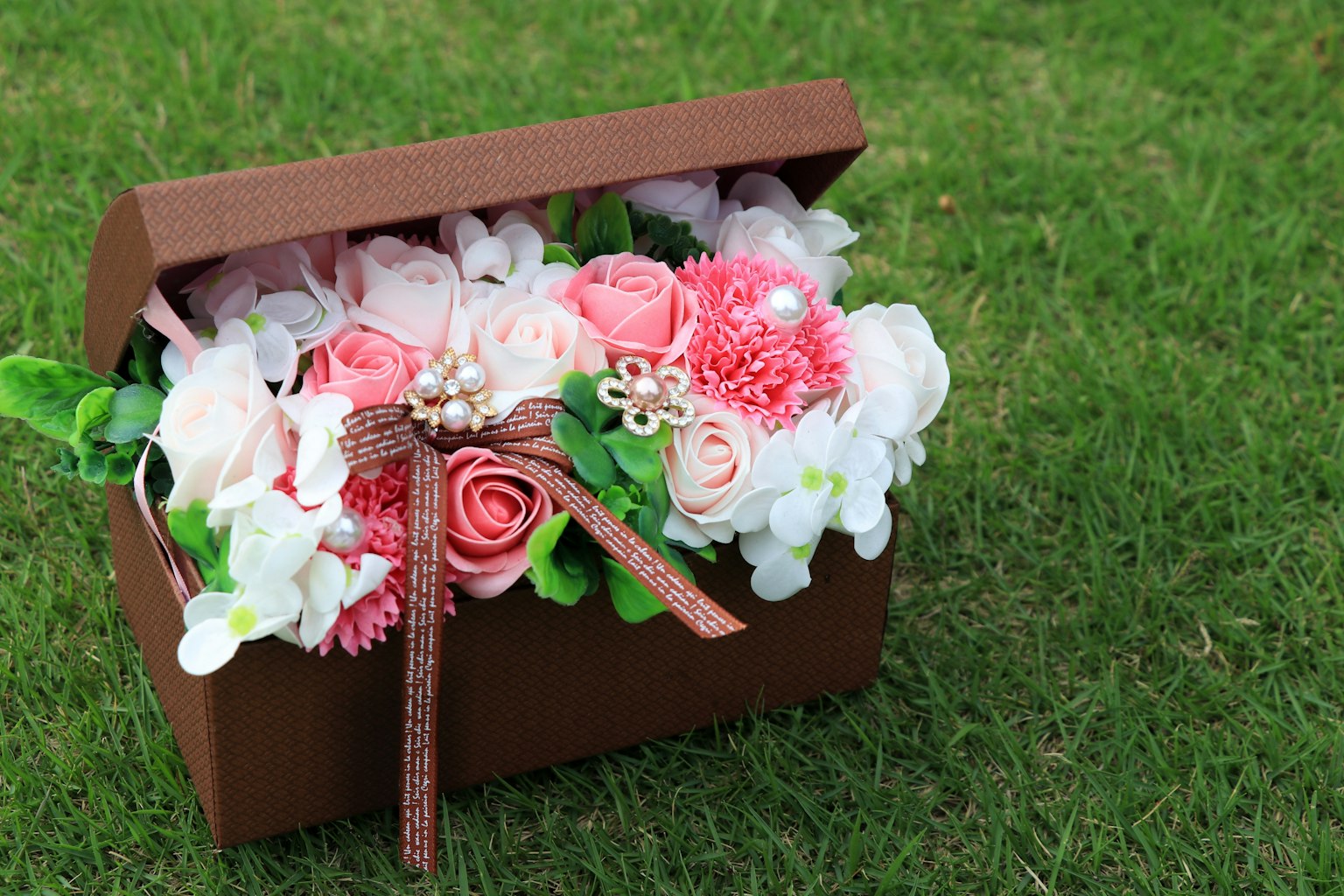 Un bouquet di fiori rosa e bianchi in una scatola marrone posato su erba verde