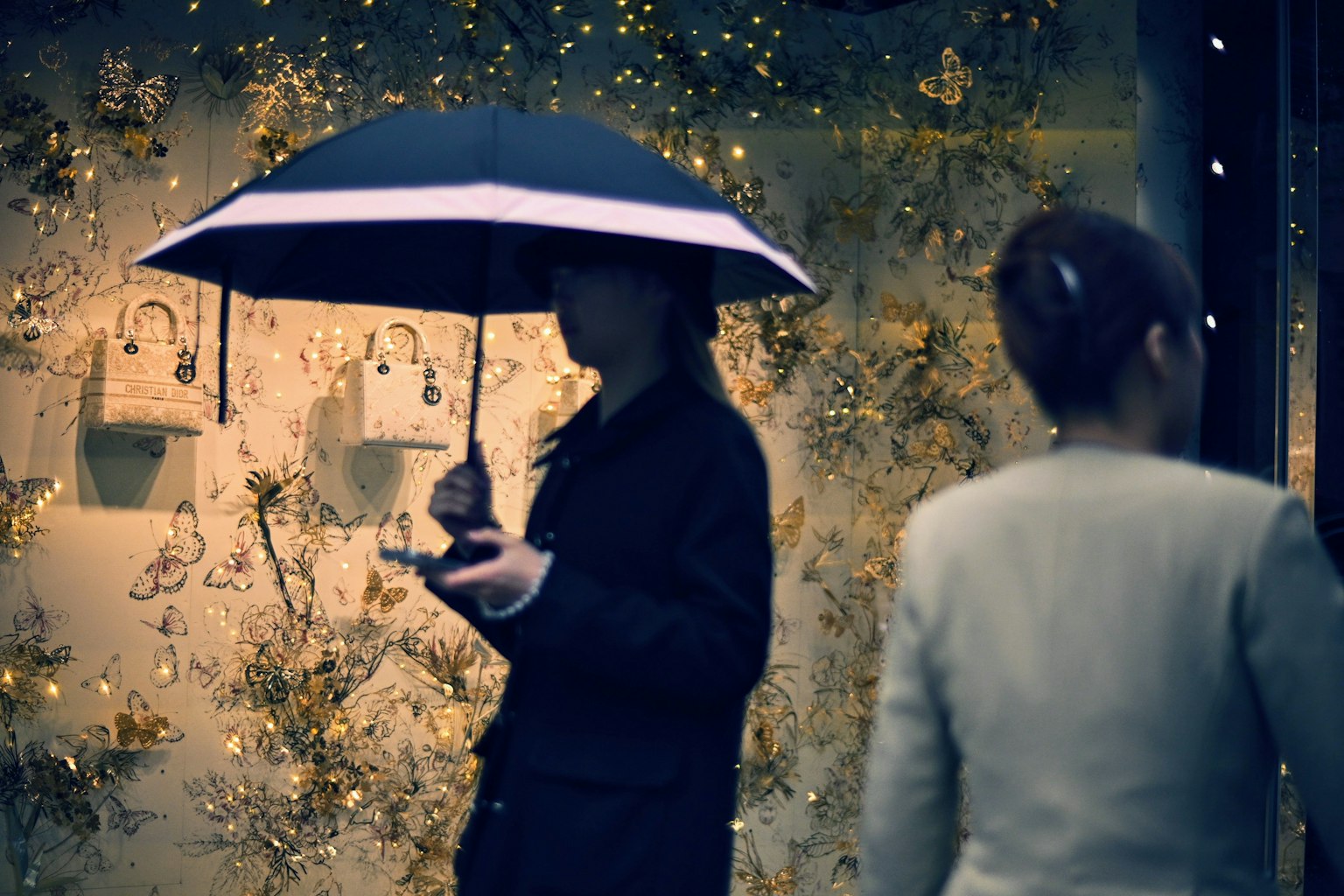 Une personne tenant un parapluie se tient devant une vitrine ornée de fleurs et de lumières
