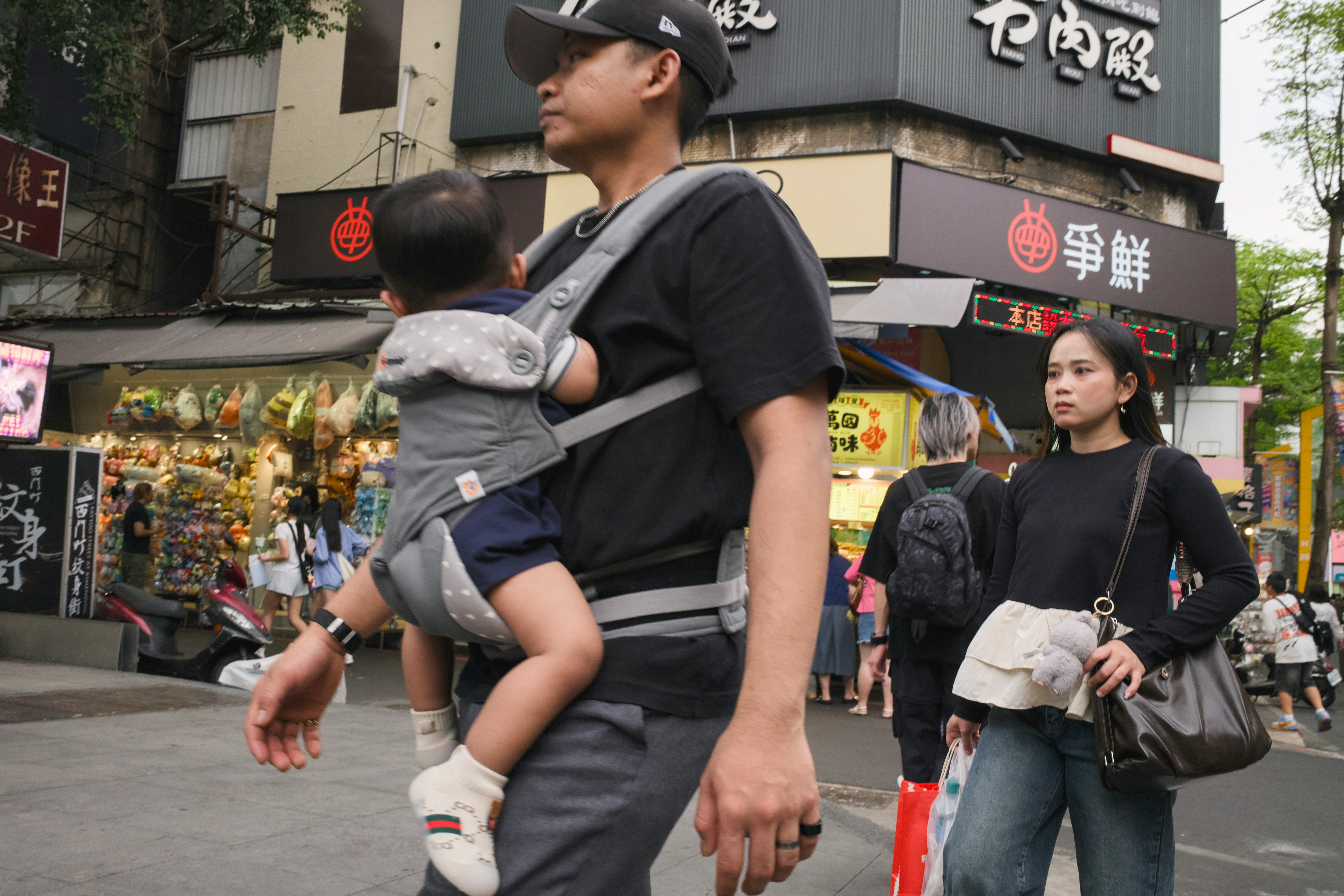 商店街の軒先で子どもを抱く親子と買い物客