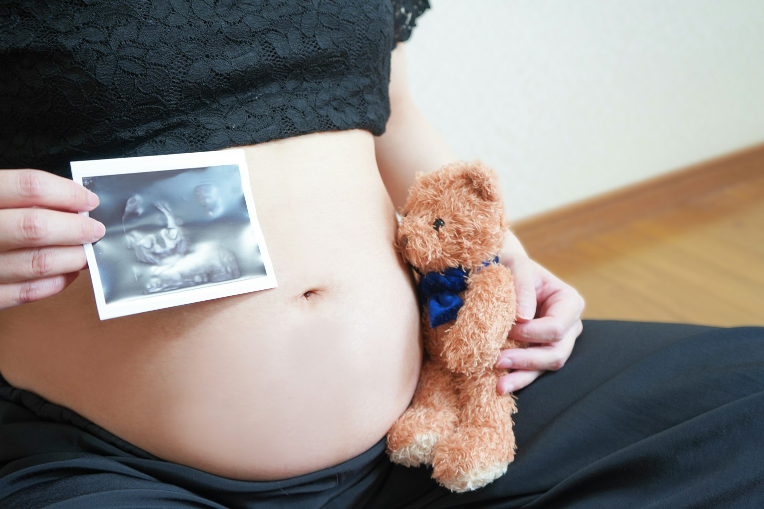 Pregnant woman holding ultrasound photo on belly with teddy bear