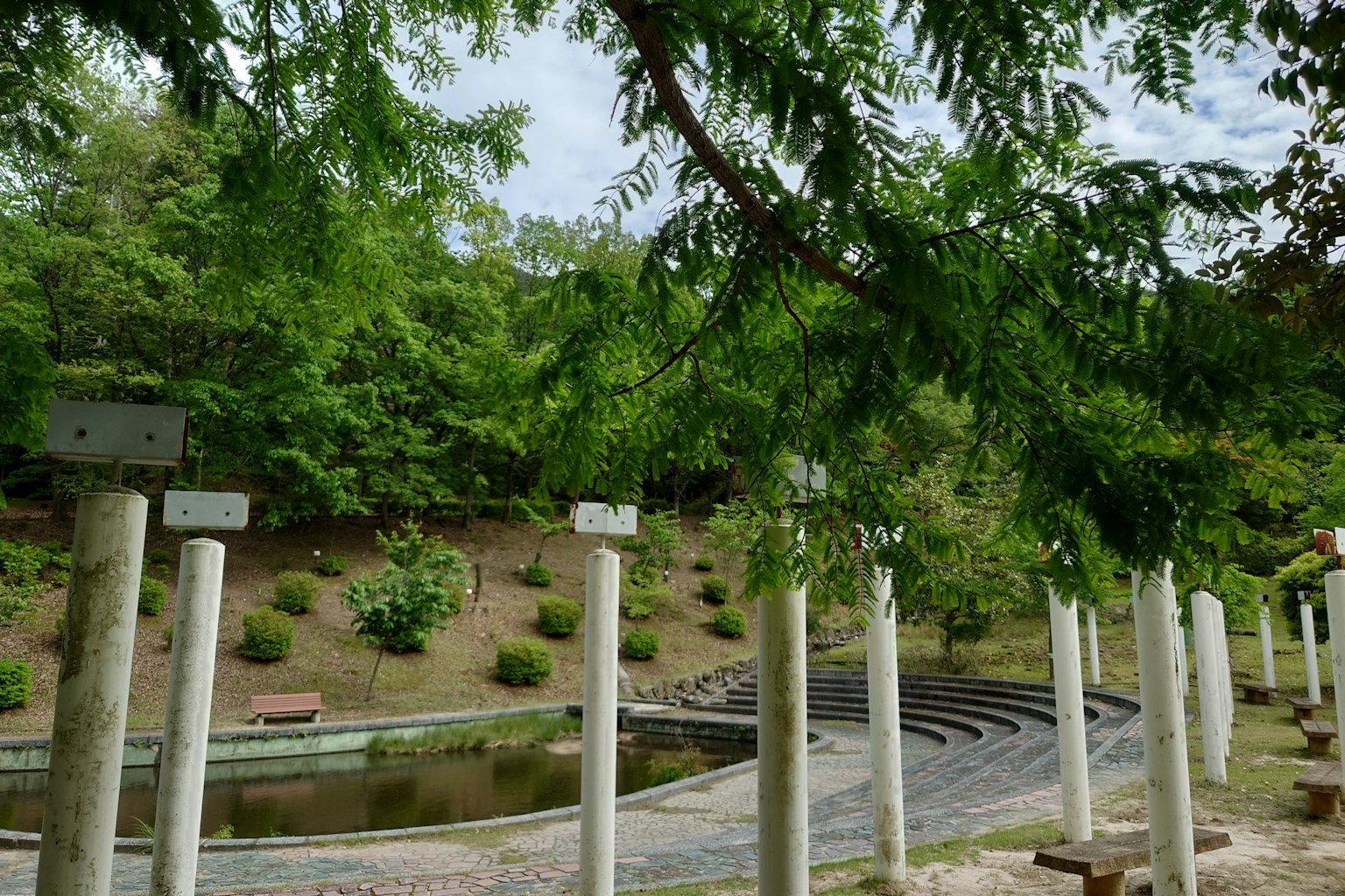 Pemandangan taman yang rimbun dengan tiang putih dan semak-semak yang rapi di sekitar kolam