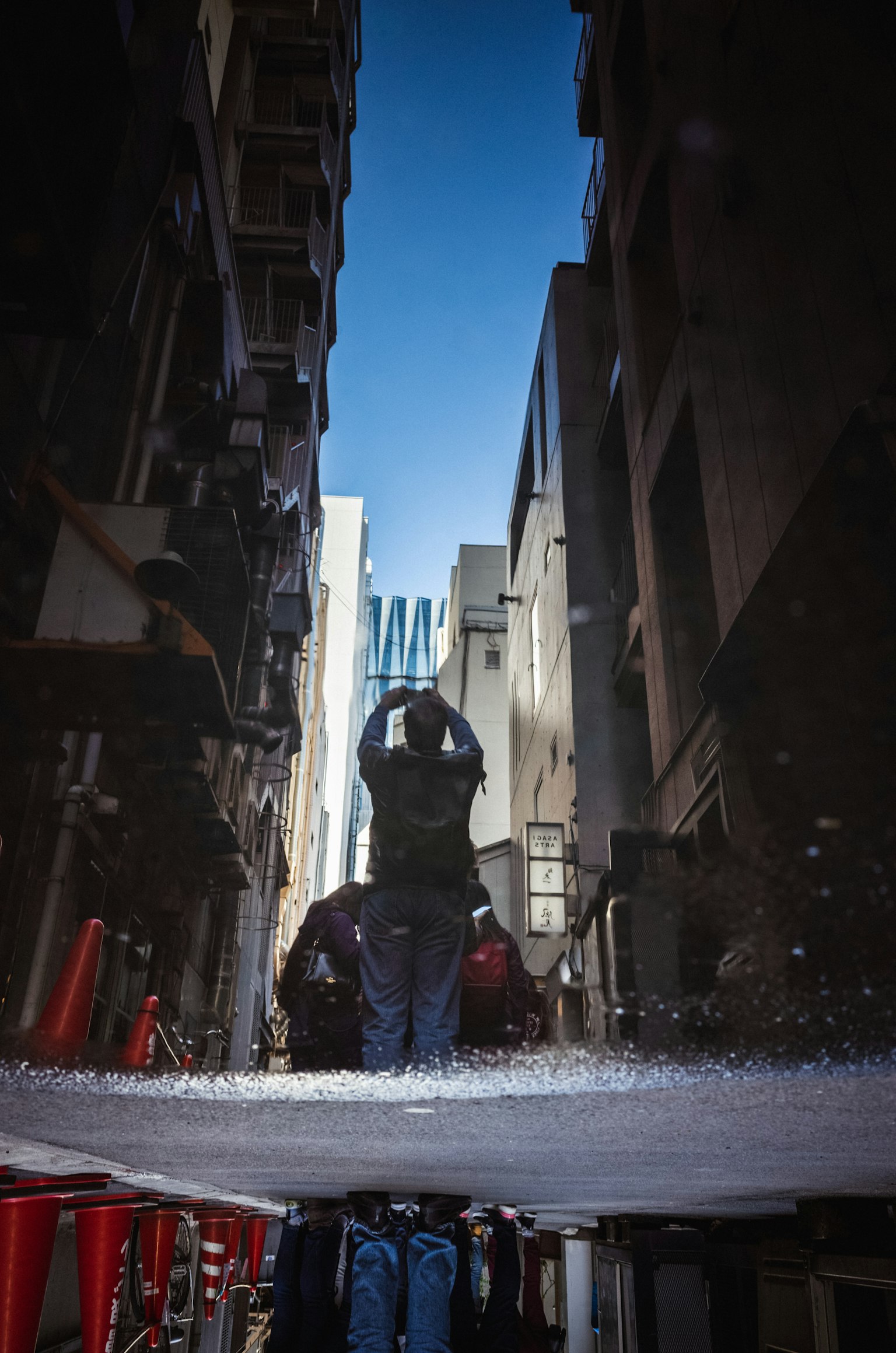 Arbeiter spritzt Wasser in einer engen Gasse mit Gebäuden auf beiden Seiten