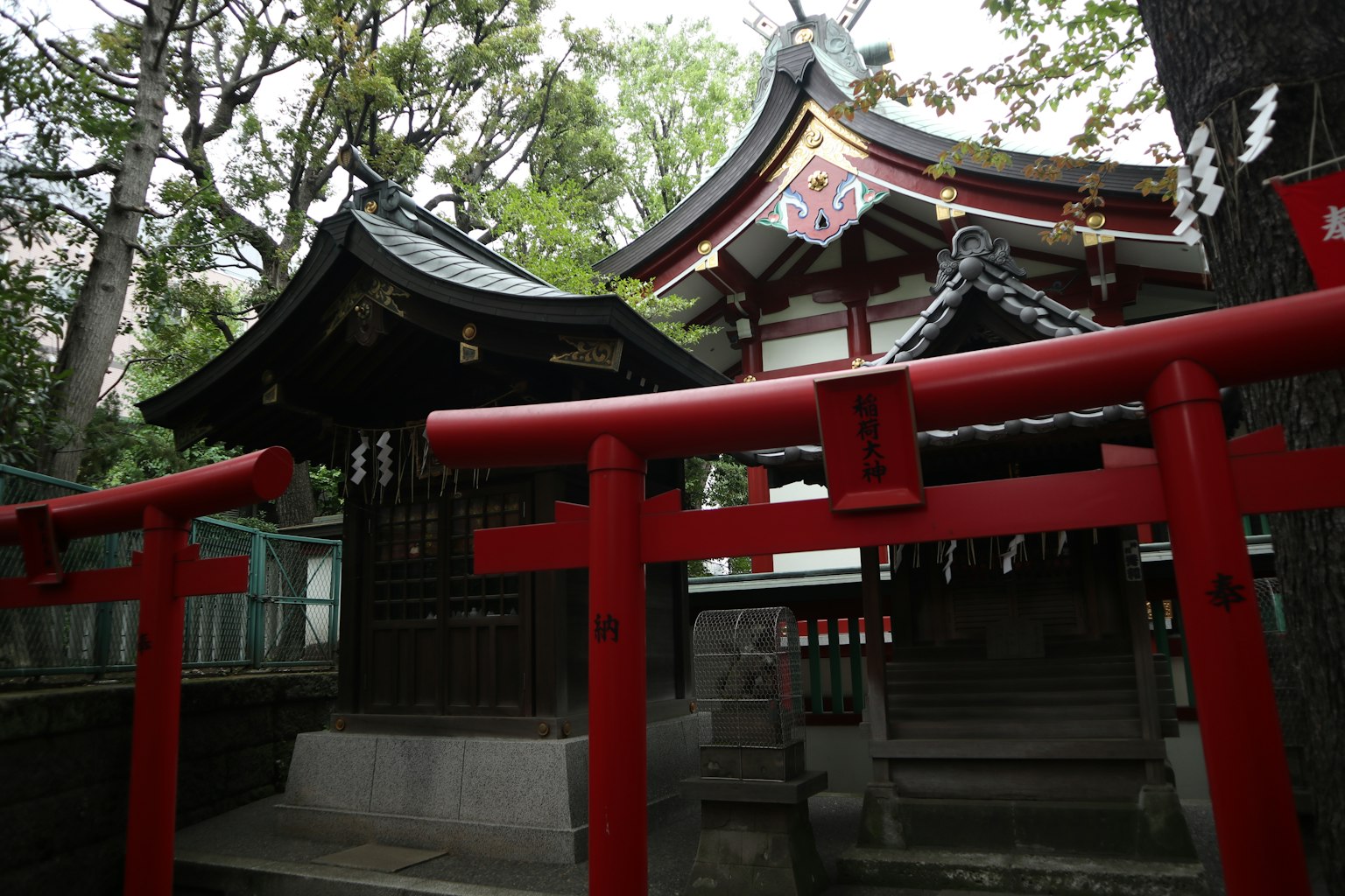Una vista panoramica con un portale torii rosso e un edificio del santuario circondato da una vegetazione lussureggiante