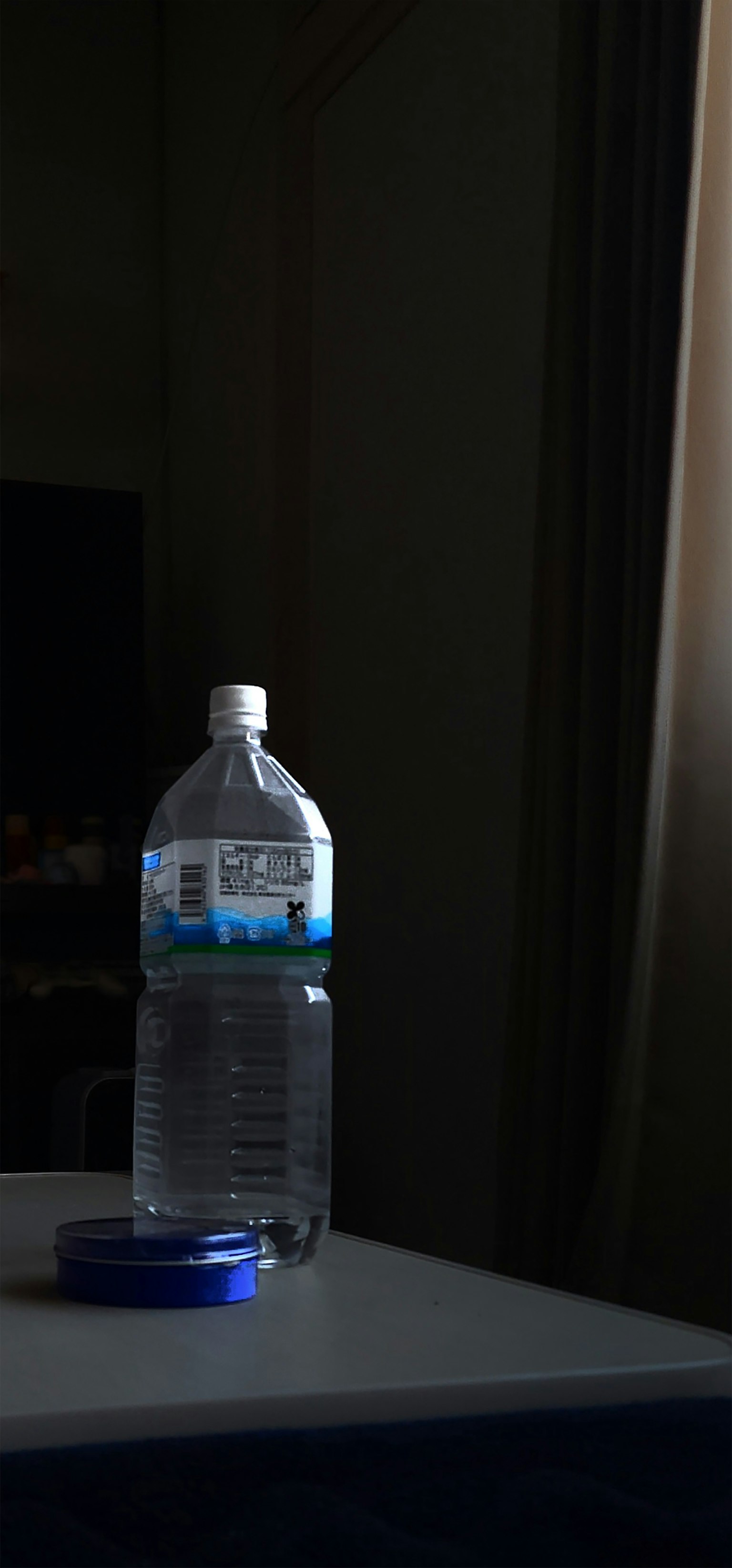 Eine Wasserflasche mit einem blauen Deckel auf einem Tisch in einem schwach beleuchteten Raum