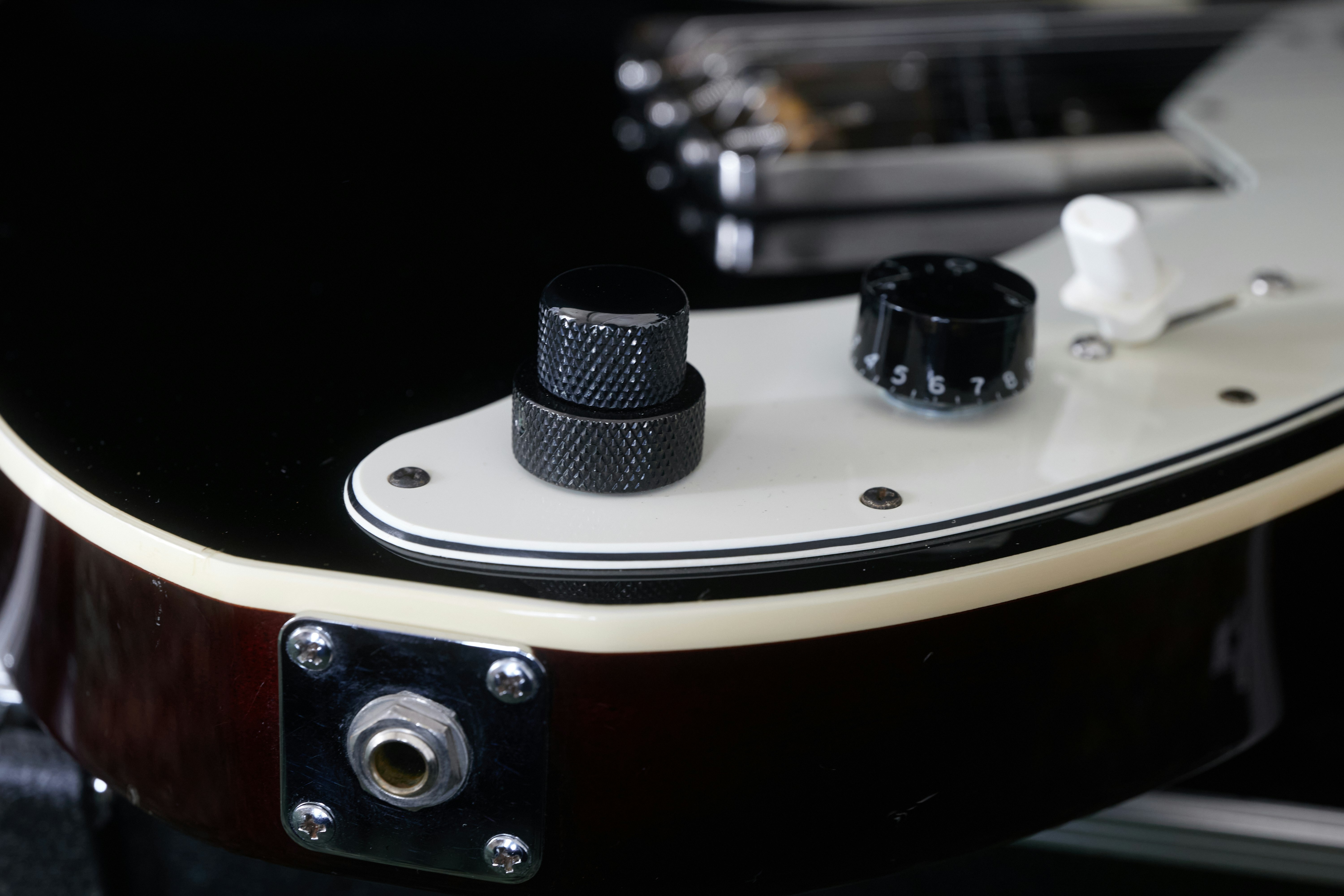 Close-up of a guitar body showing black and white knobs and a jack