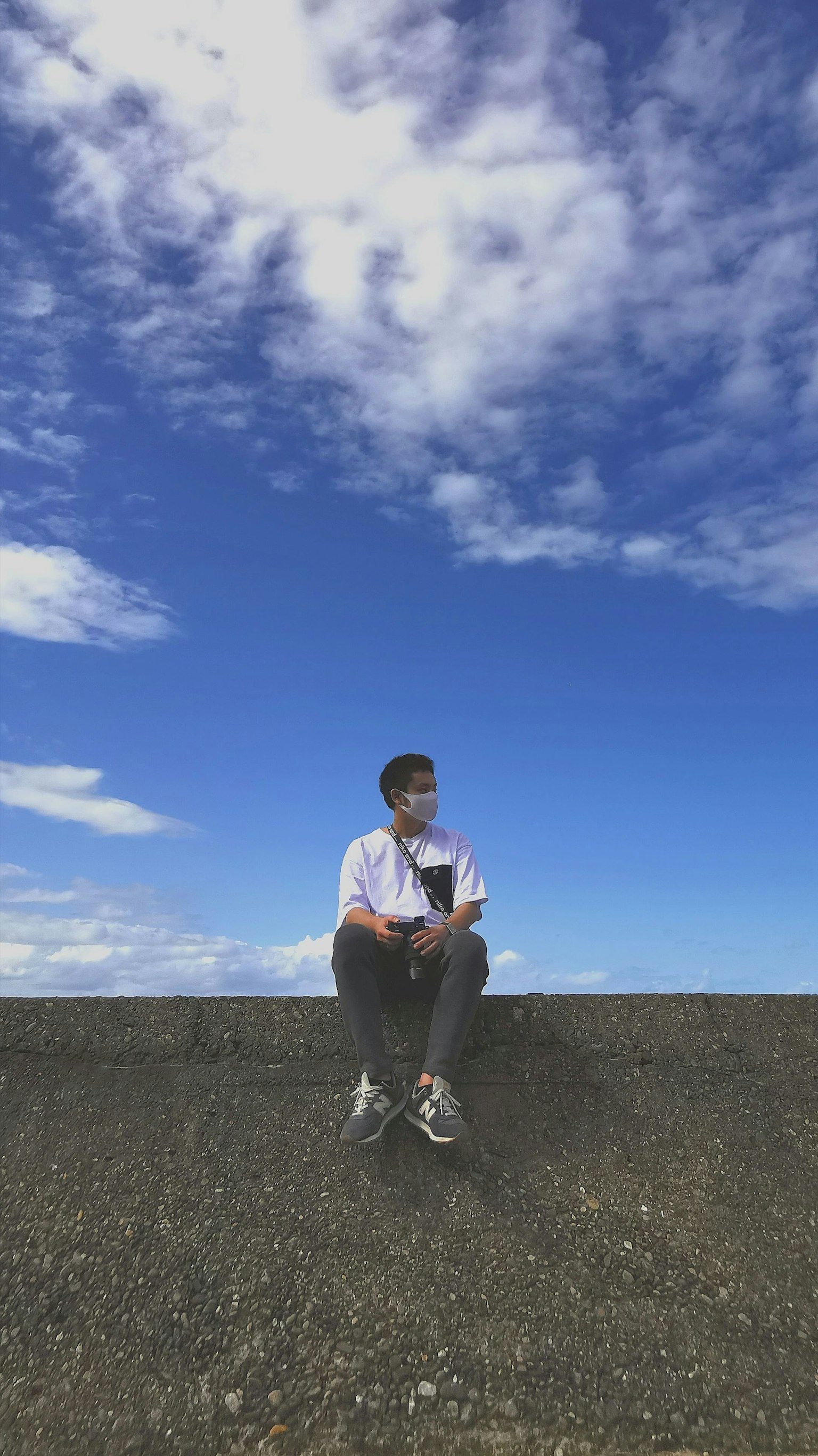 藍天下坐在牆上的男人 他穿著白襯衫和黑褲子