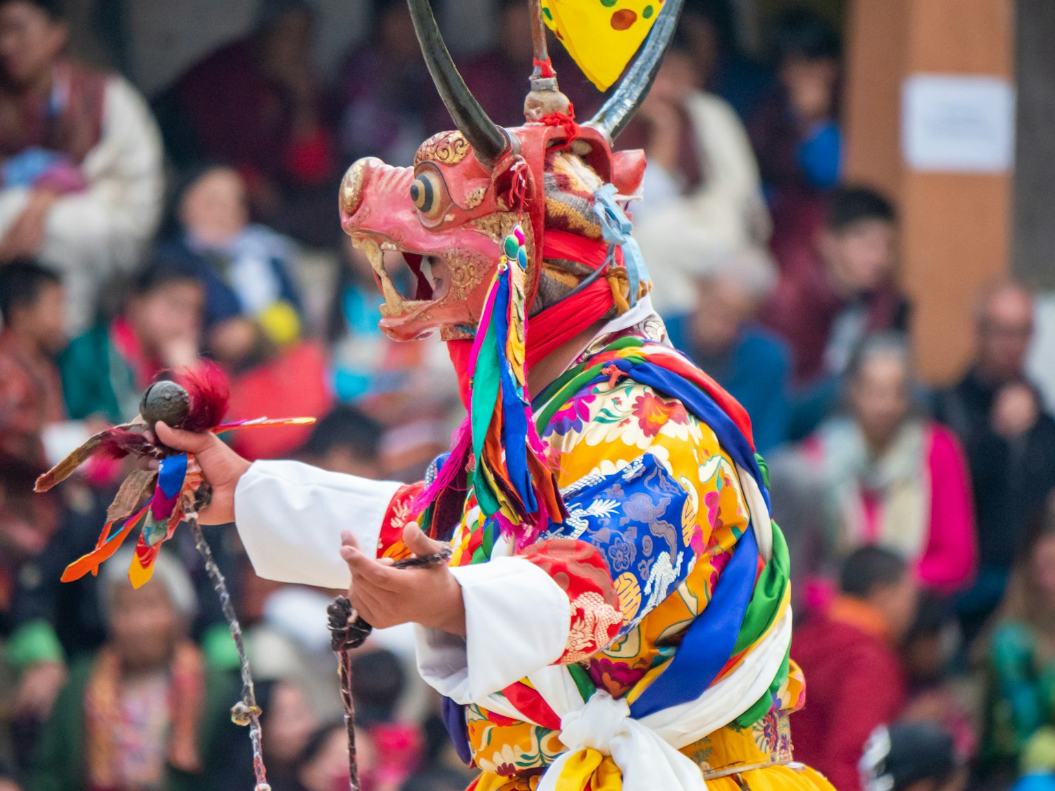 Un performer che indossa una maschera tradizionale e un abbigliamento colorato si esibisce di fronte a un pubblico