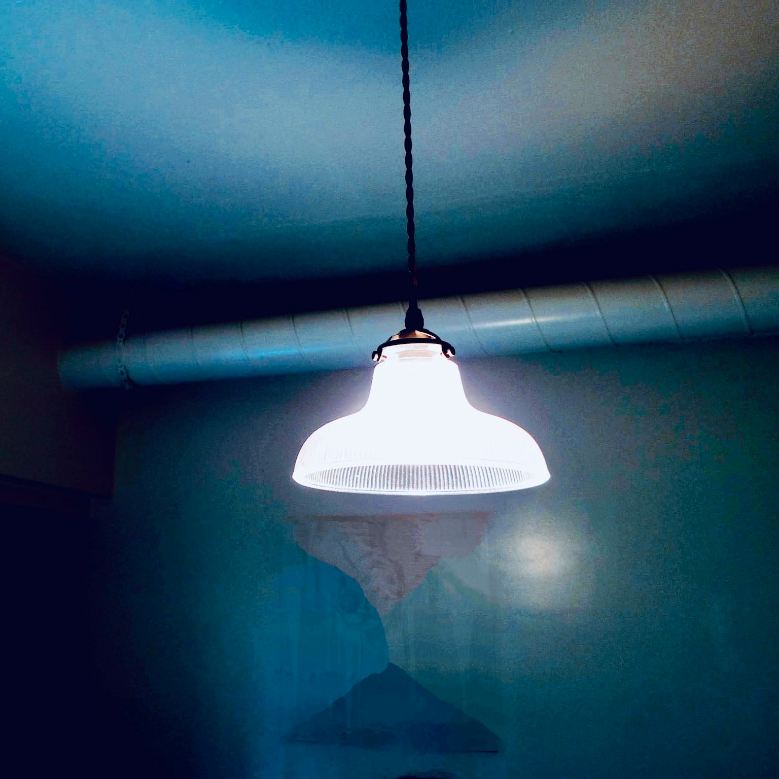 A white pendant light hanging against a blue background in a simple interior