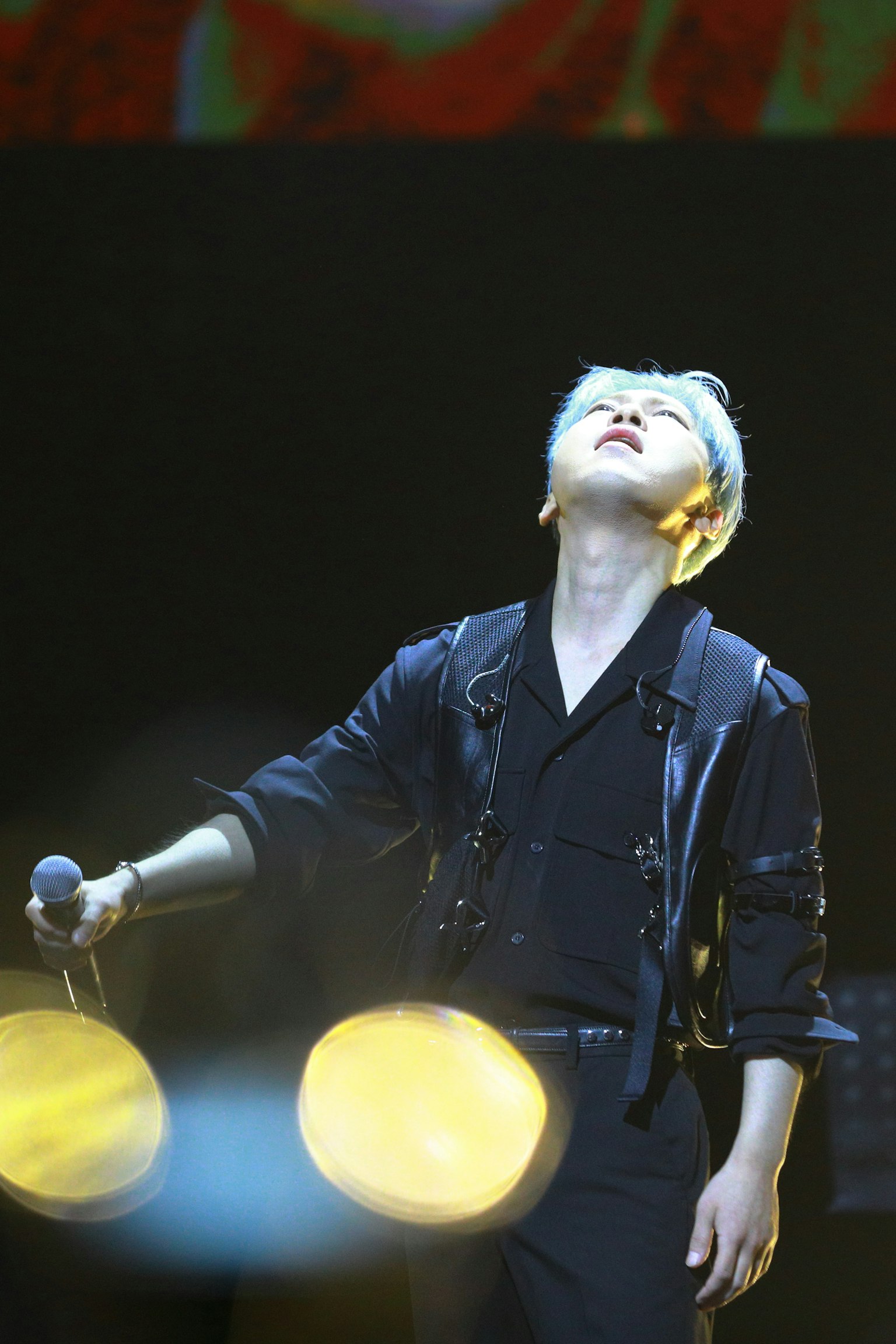 Un homme aux cheveux bleus se produisant sur scène tenant un microphone