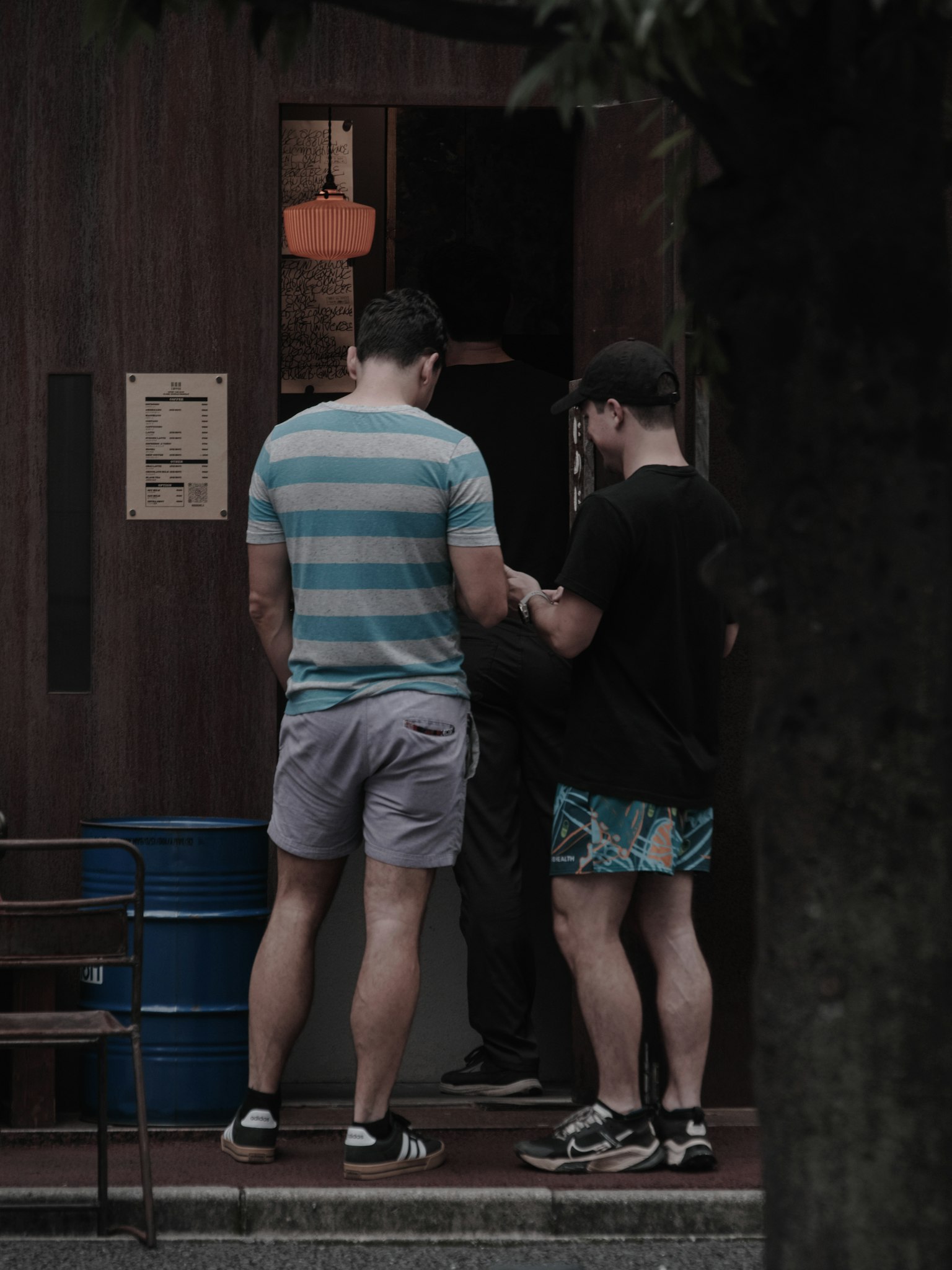 ชายสองคนในชุดลำลองกำลังพูดคุยอยู่หน้าตึกมีต้นไม้ในพื้นหลัง