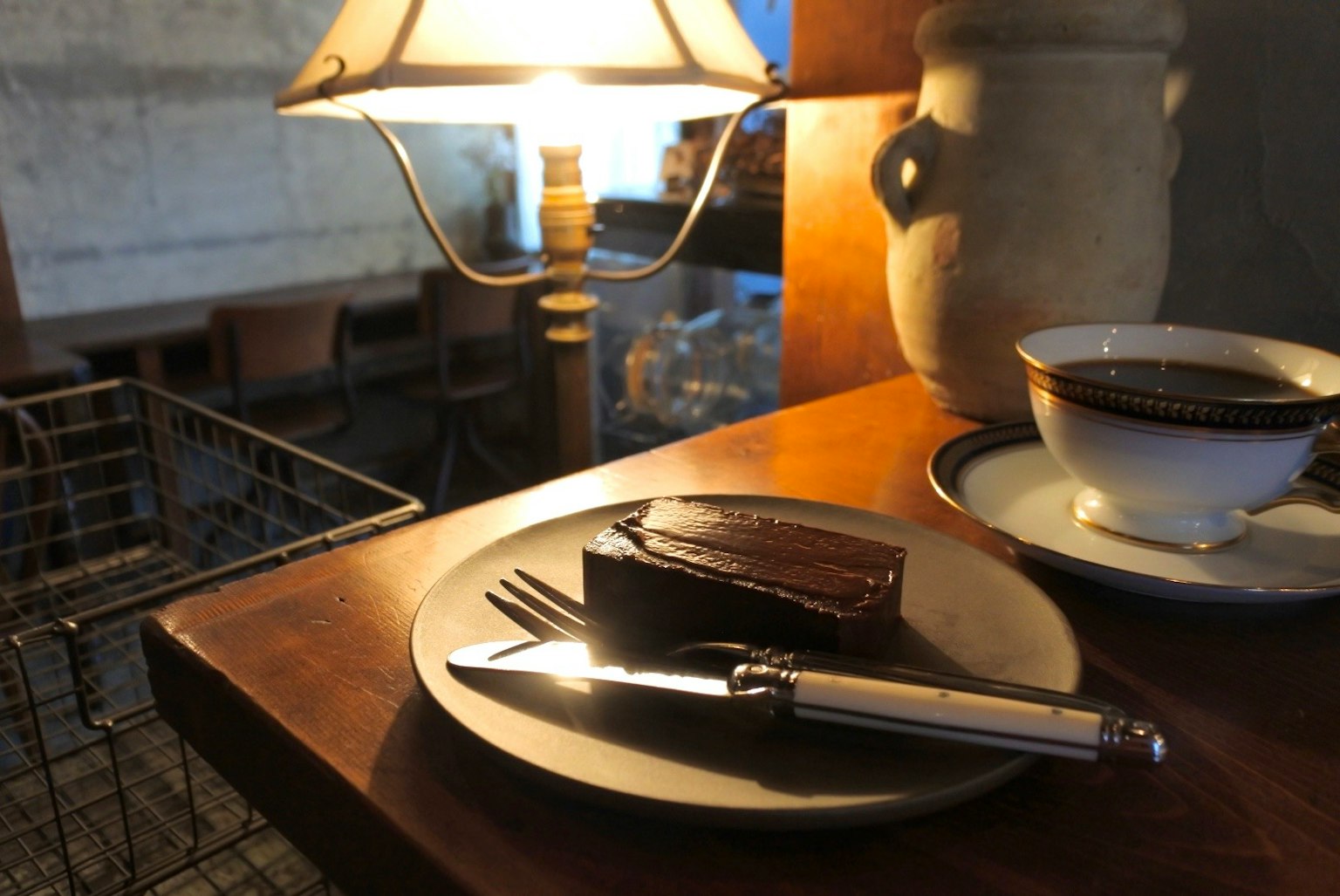 จานกาแฟและเค้กบนโต๊ะไม้แสงไฟอุ่นๆ ส่องสว่างบรรยากาศคาเฟ่ที่อบอุ่น