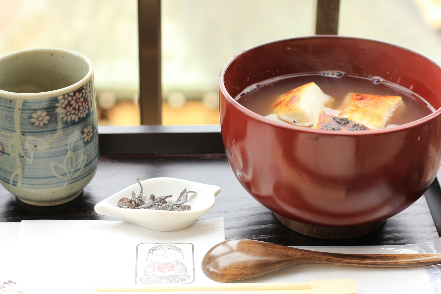 Sopa de miso en un tazón rojo con té verde en una taza azul junto a la ventana