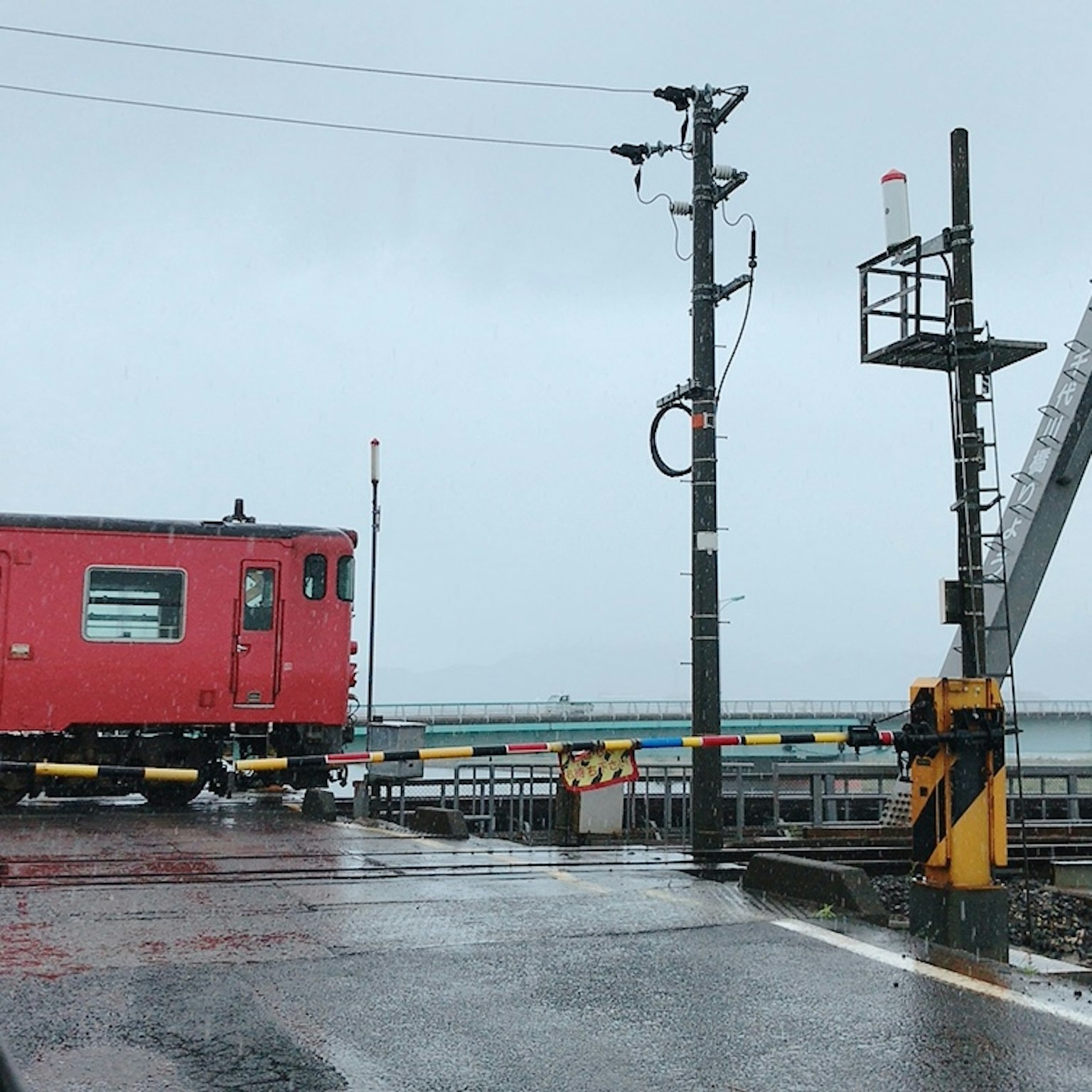 Gerbong kereta merah dan menara sinyal di hari hujan di perlintasan kereta