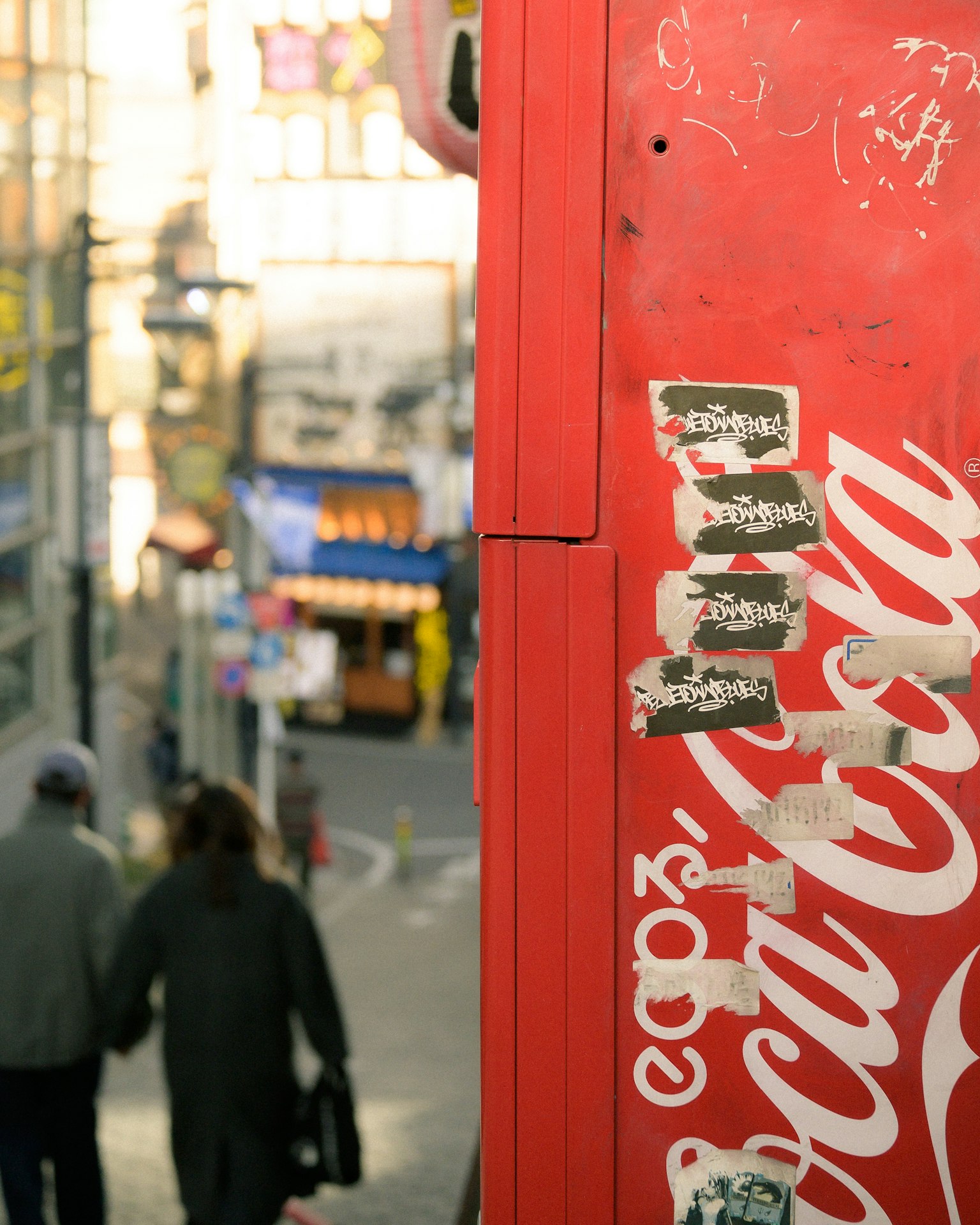 Distributore automatico Coca-Cola rosso con una coppia che cammina per strada