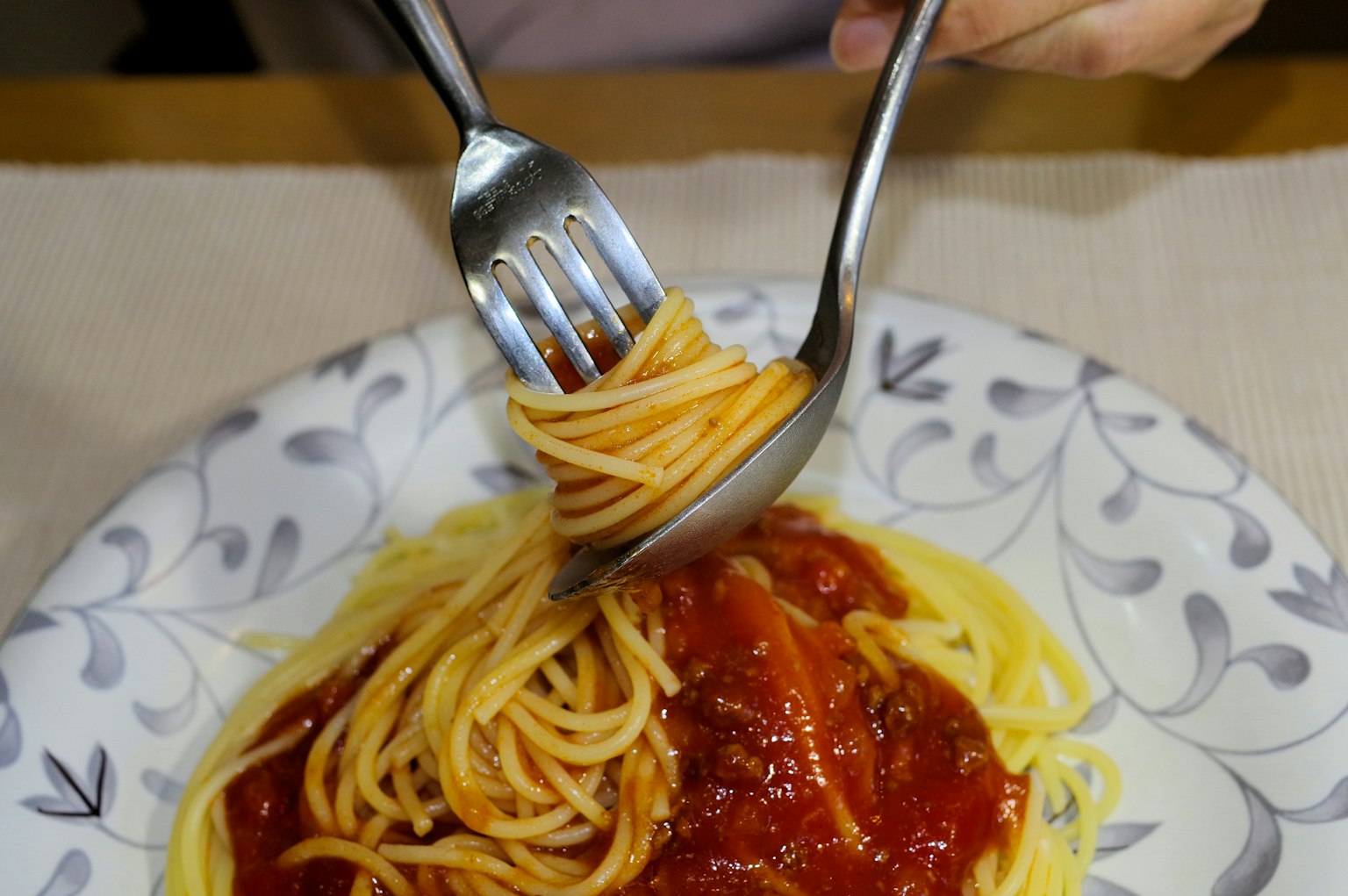 A plate of spaghetti being twirled with a fork and spoon in tomato sauce