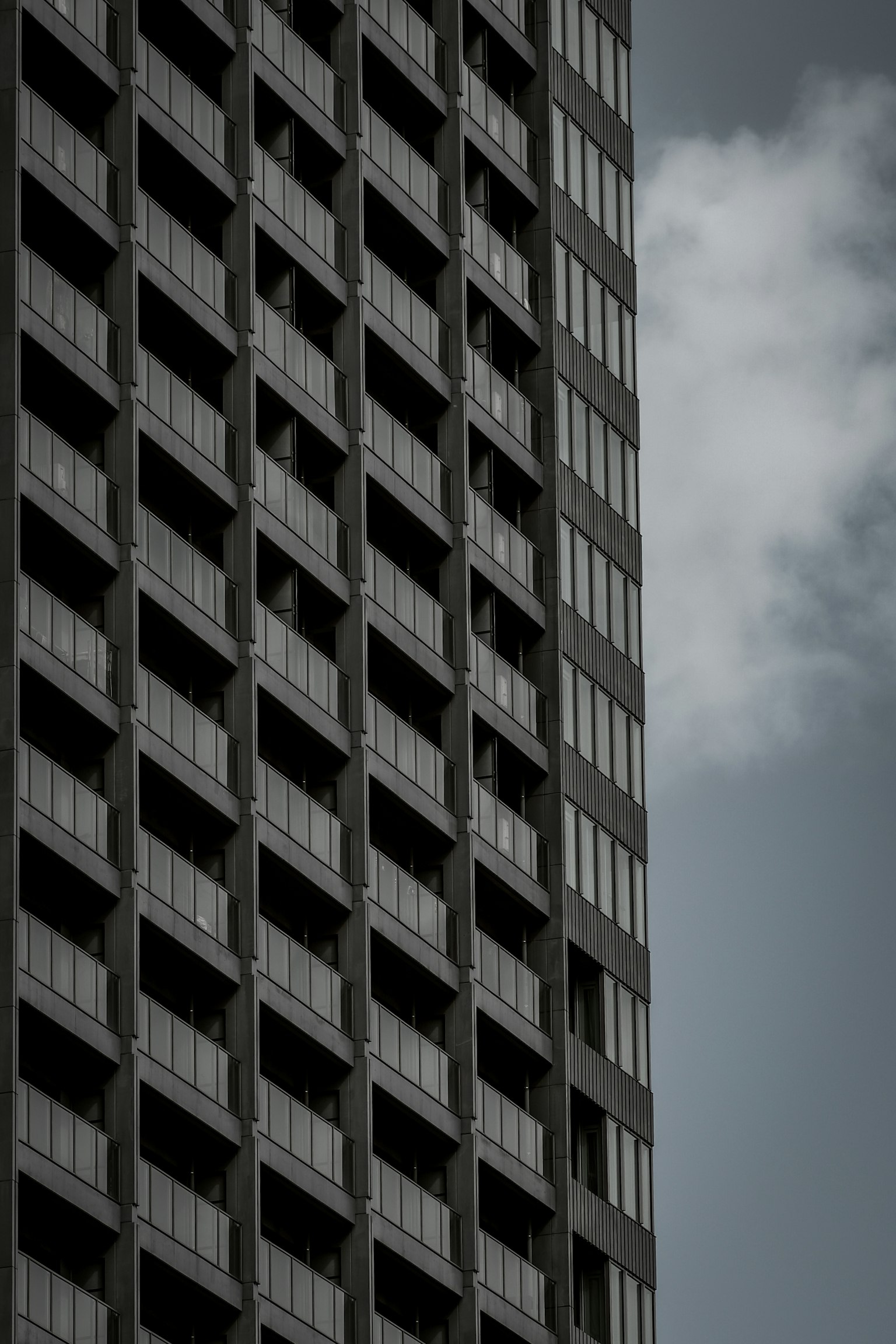 Image of a high-rise building side featuring a black facade with rows of windows and a hint of blue sky