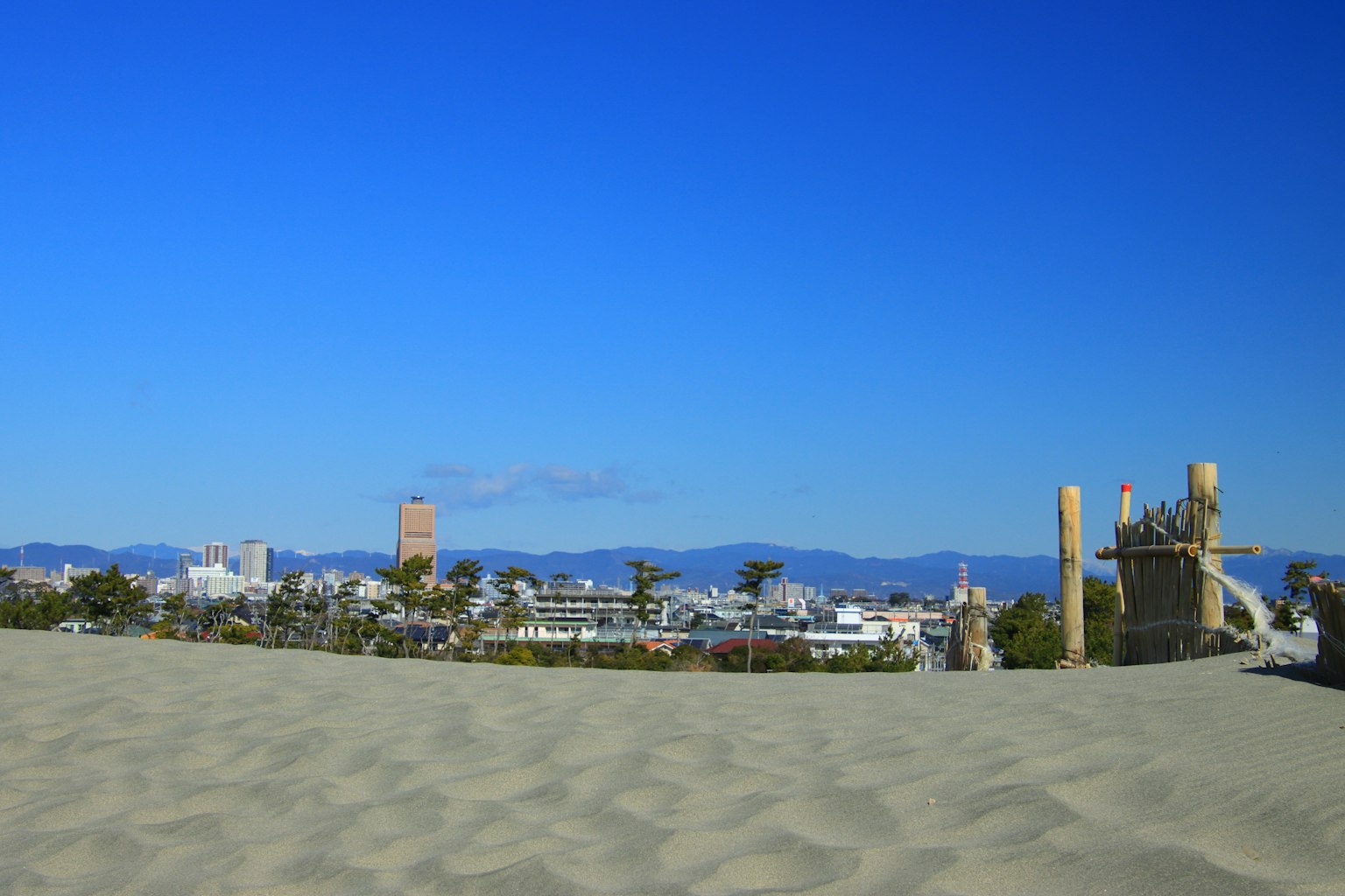 Landschaft mit blauem Himmel und Sanddünen sowie einer Stadtsilhouette im Hintergrund