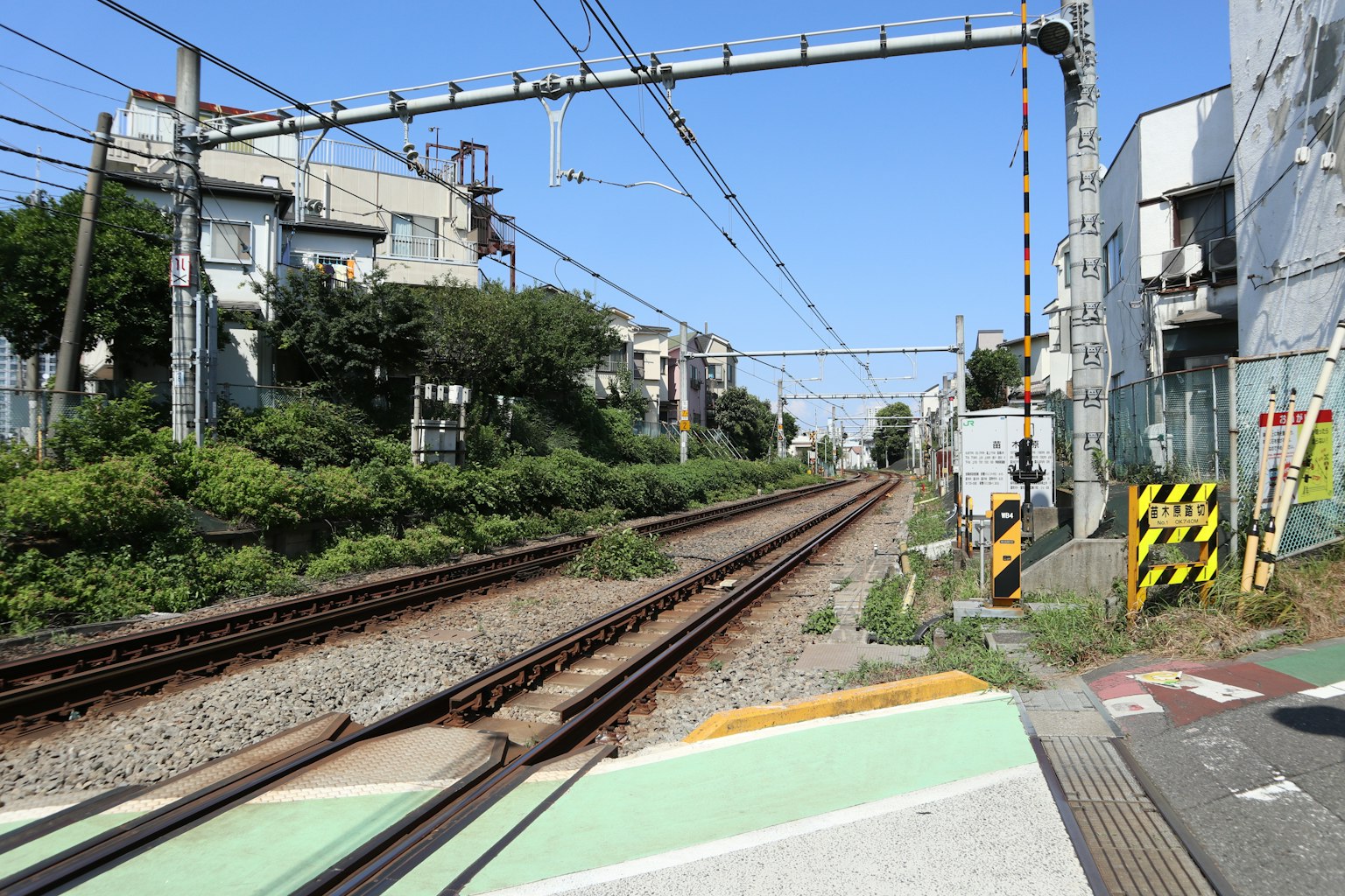 Train tracks with surrounding buildings and greenery under a clear blue sky